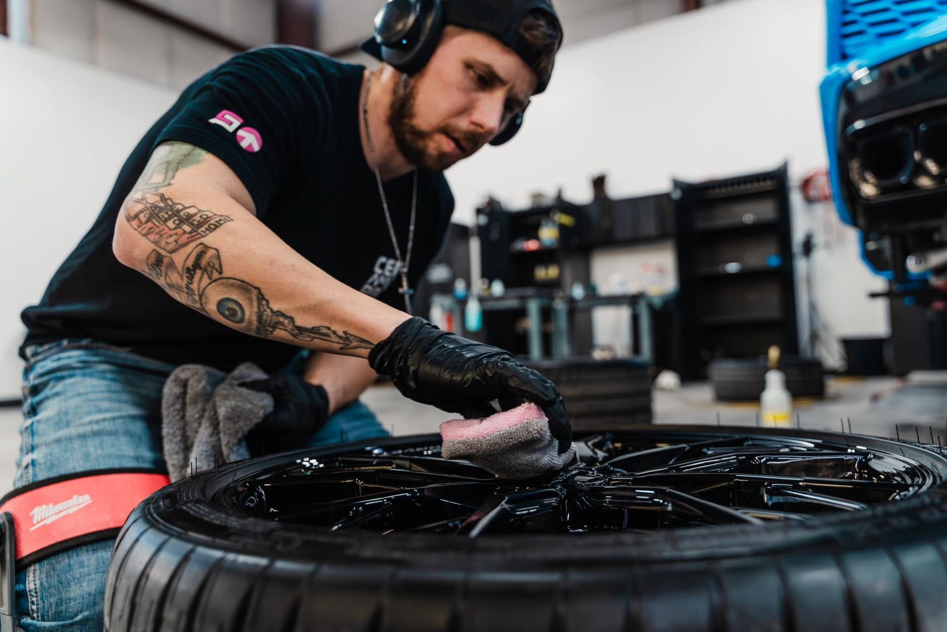 Mechanic wearing headphones and gloves cleans a car tire in a workshop