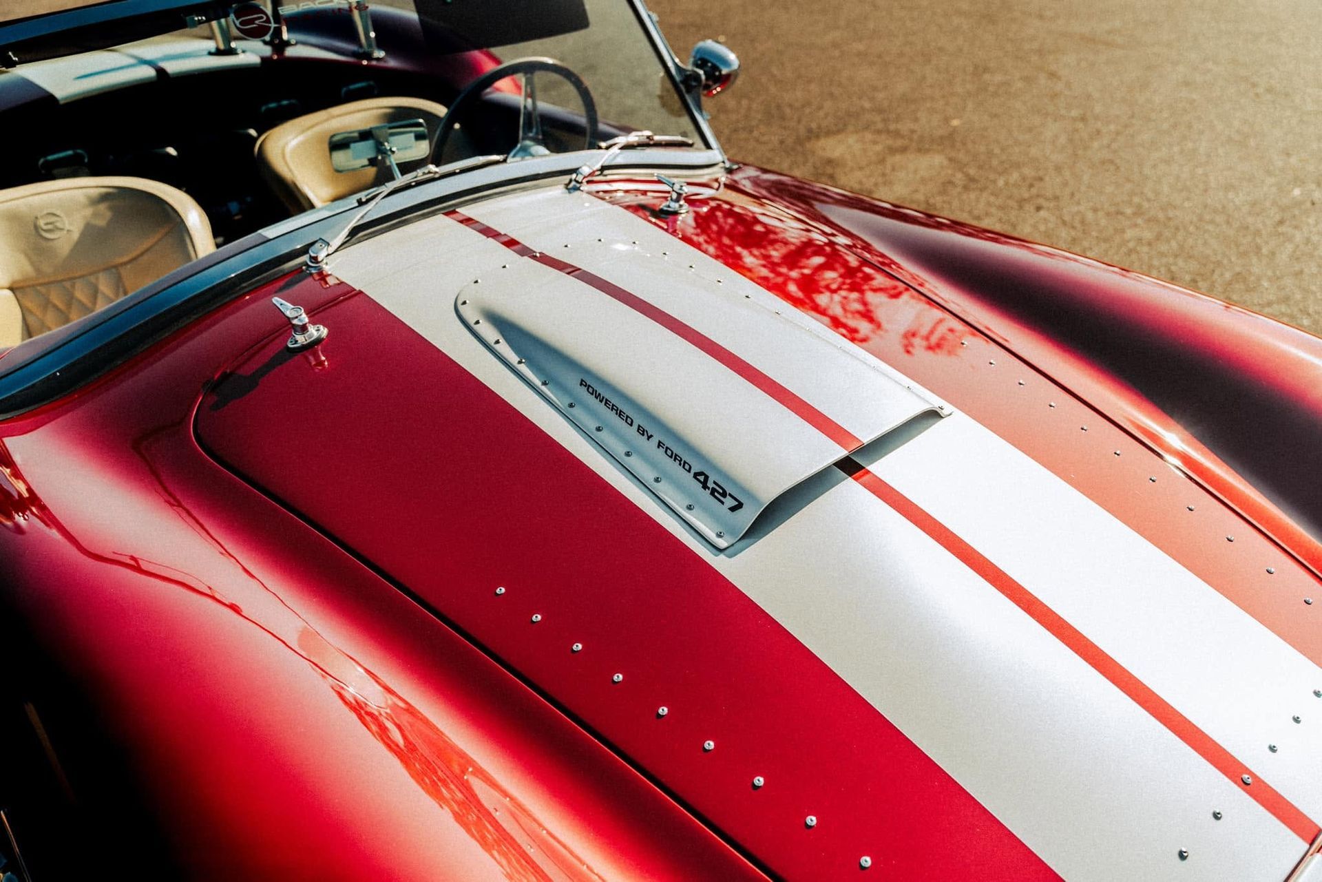 Close-up of a red classic car hood with white racing stripes and chrome scoop.