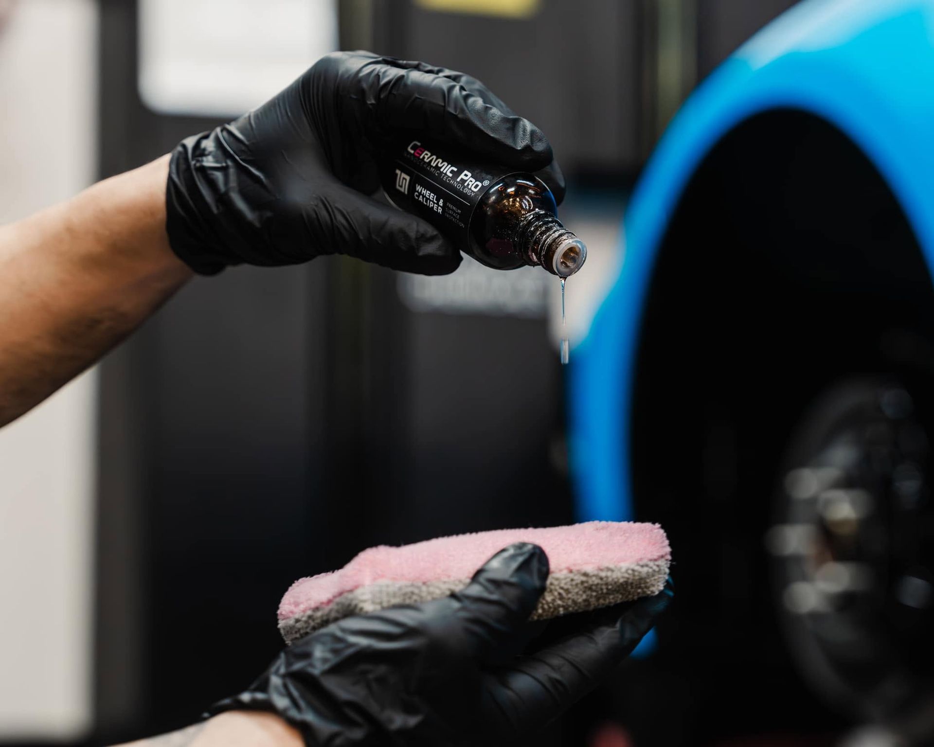 Gloved hands applying polish to a car’s blue exterior with a sponge