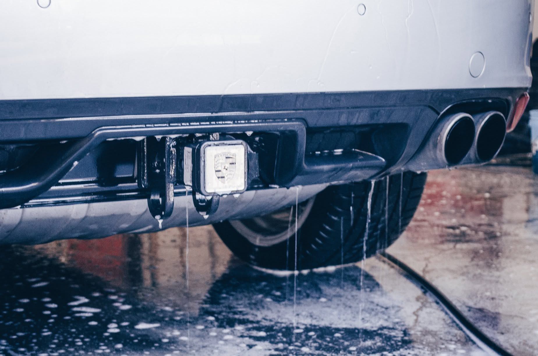 Rear view of a wet car at a car wash with water spraying around the bumper and exhaust pipes