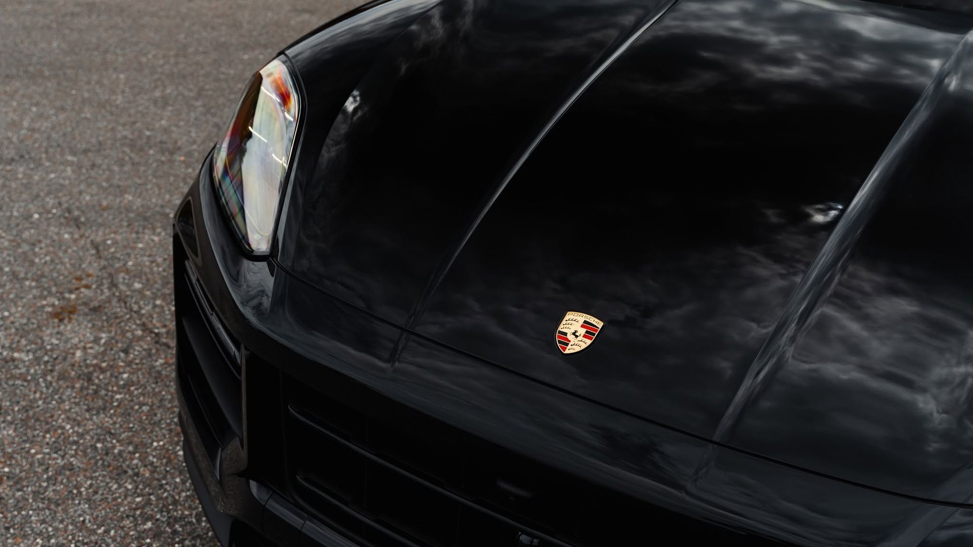 Close-up of a black Porsche hood with the crest emblem on a gray road