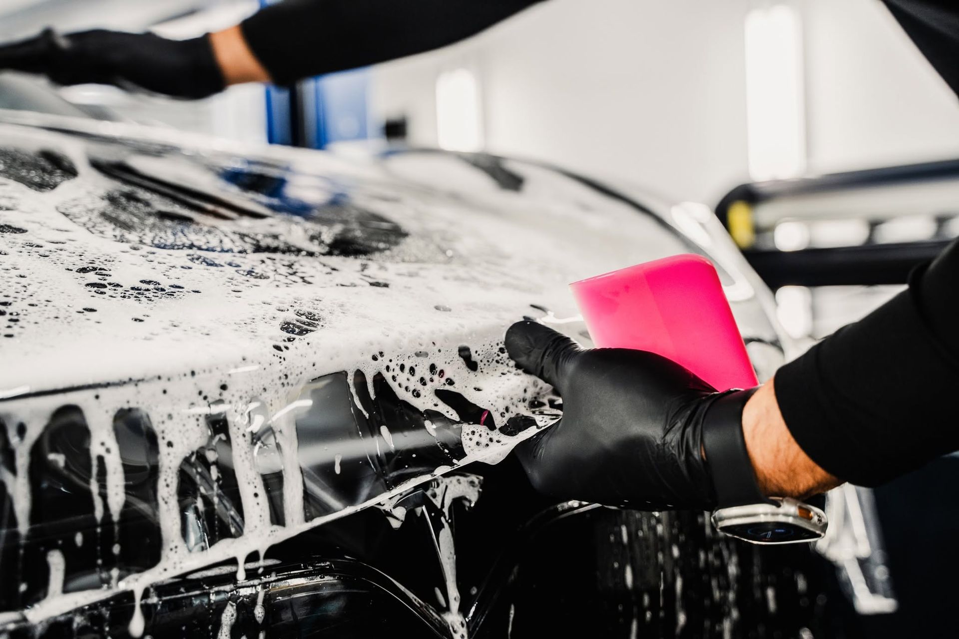 Person washing a car with thick soap suds and a pink sponge