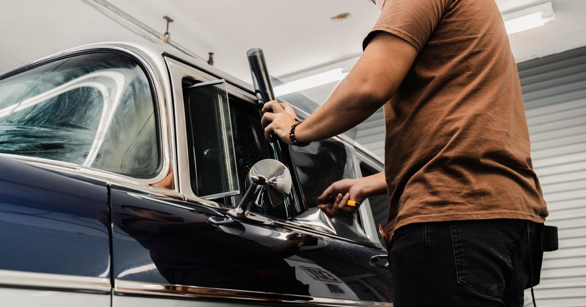 Person polishing a dark blue classic car in a garage with a power buffer