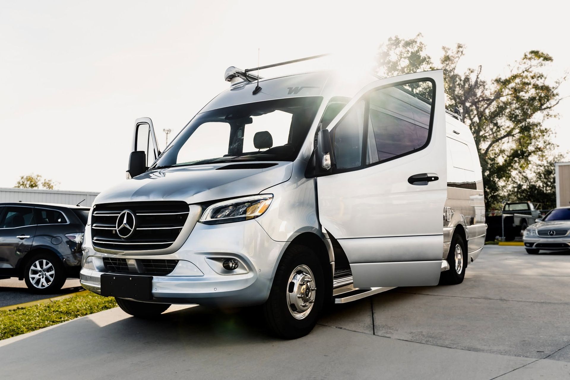 White Mercedes van parked on a sunny driveway with trees and other cars in the background