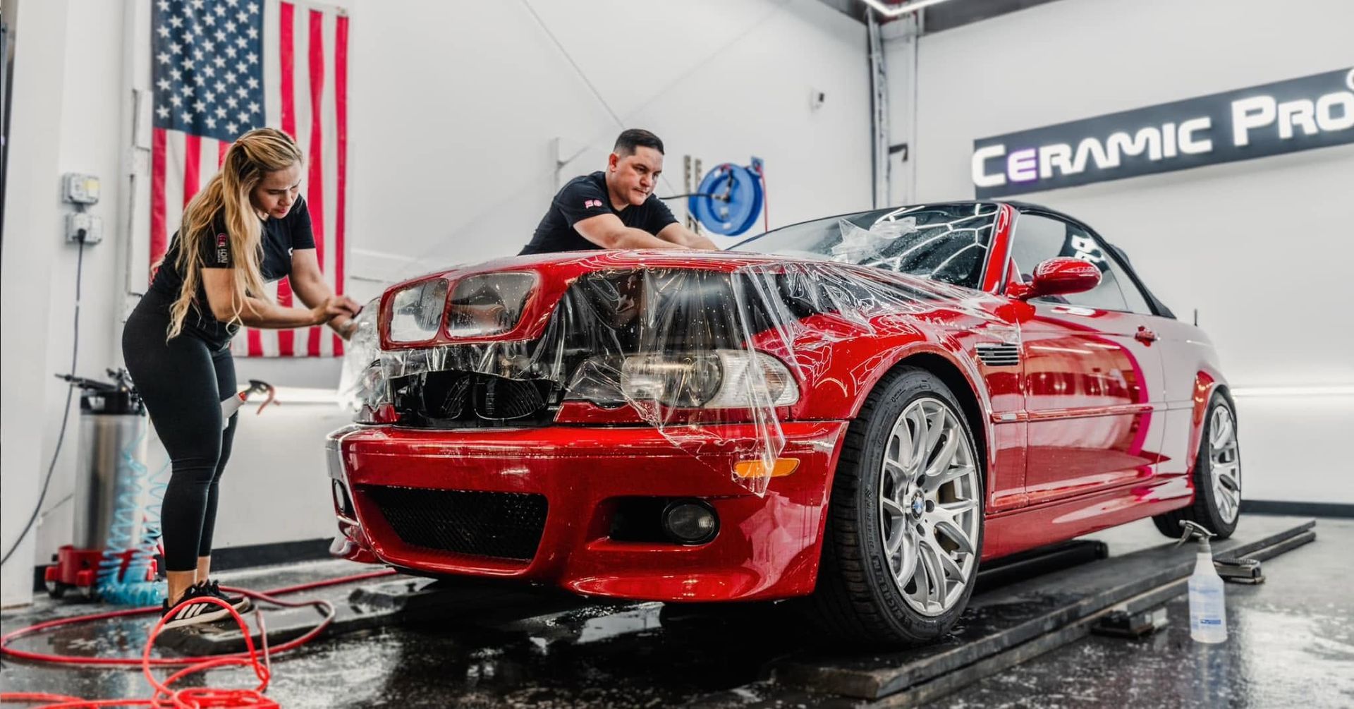 Red sports car being hand washed in a detailing garage by two workers