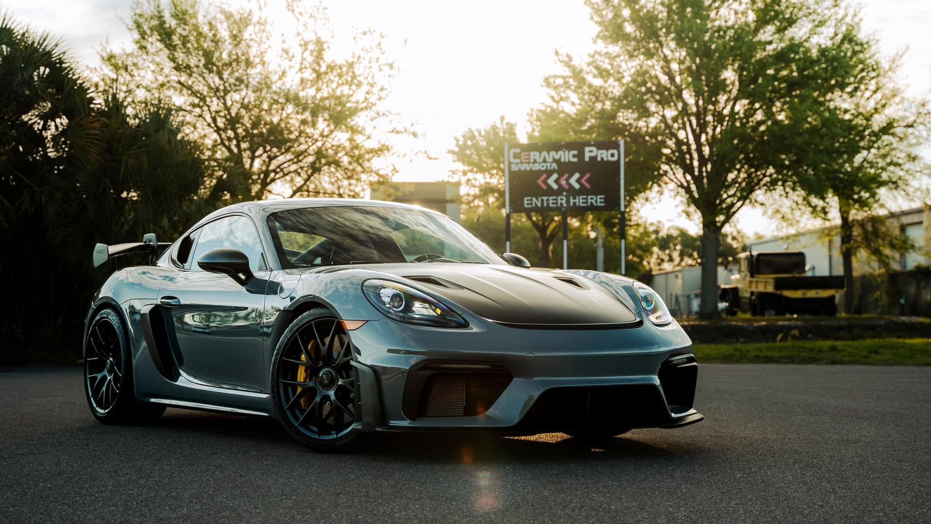 Silver sports car parked on a road at sunset with trees and a sign in the background