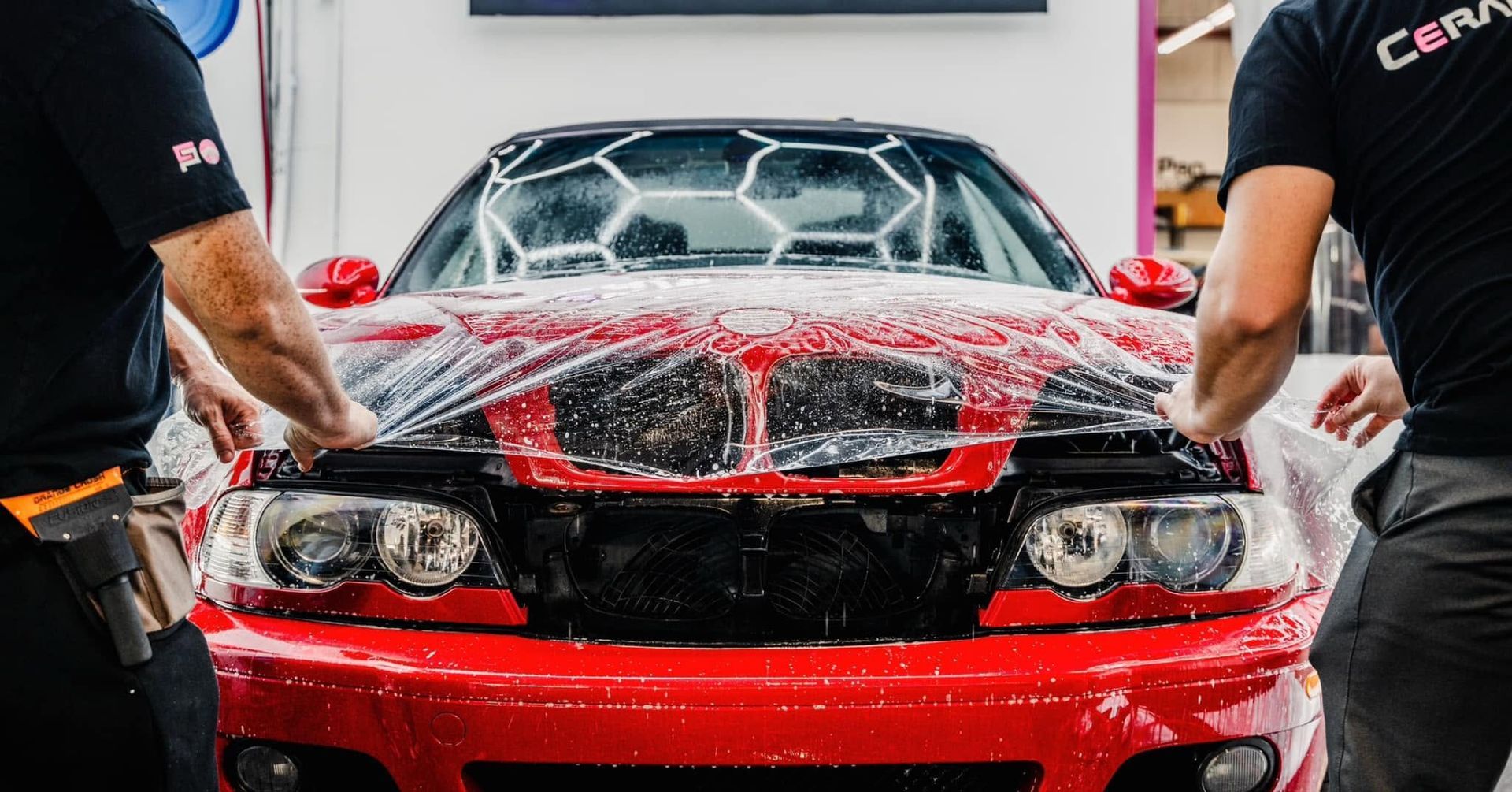 Red sports car being washed with water spray by two people in a garage