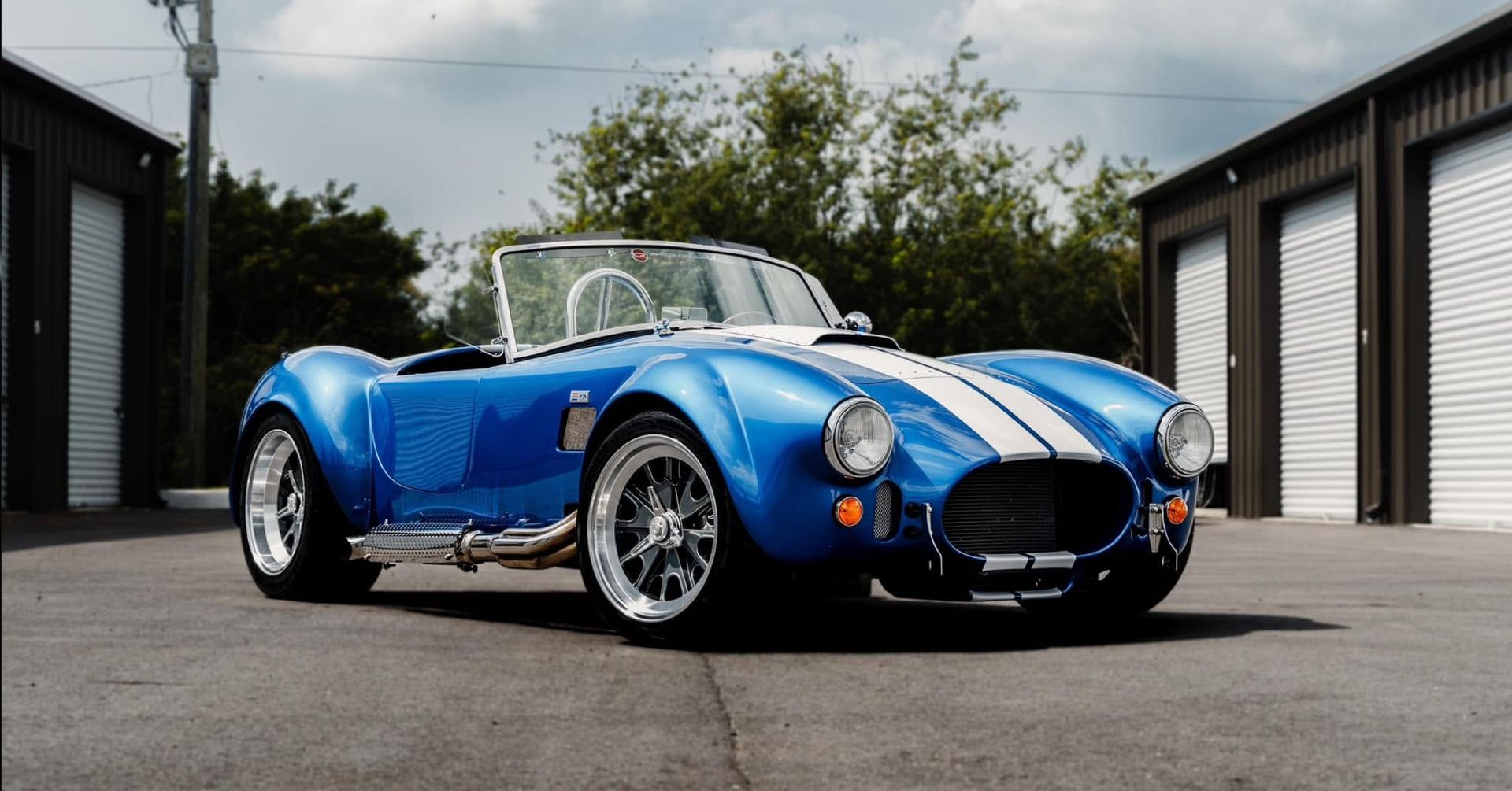 Blue classic convertible sports car parked between garages outdoors.