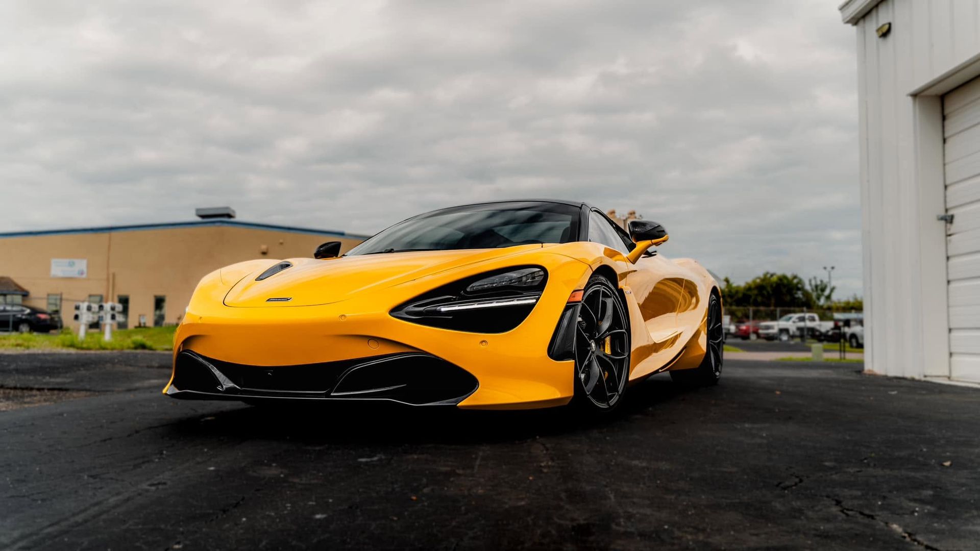 Yellow sports car parked on wet pavement outside a building under a cloudy sky