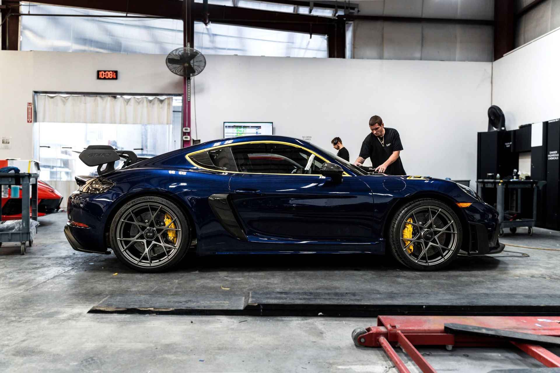 Blue sports car in an auto shop, with a person working beside it on a lift.