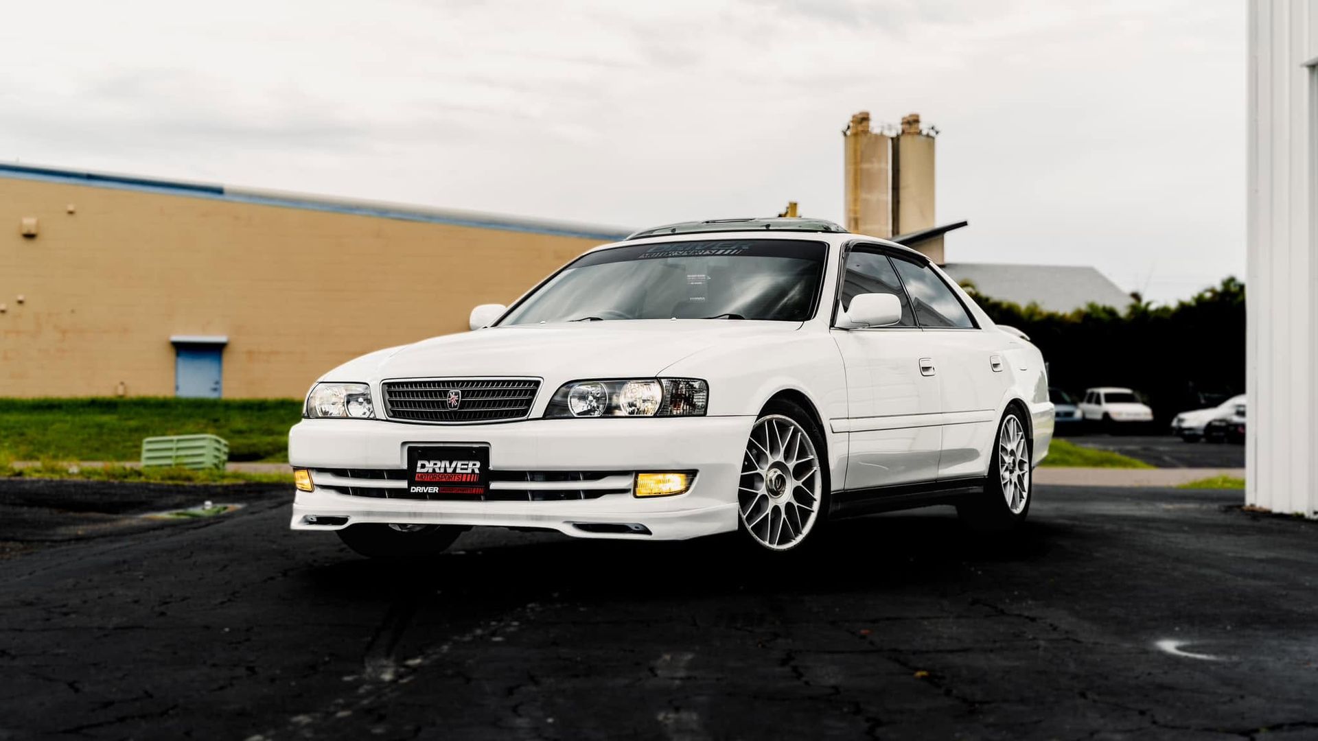 White sedan parked on wet pavement in front of a beige building at dusk.