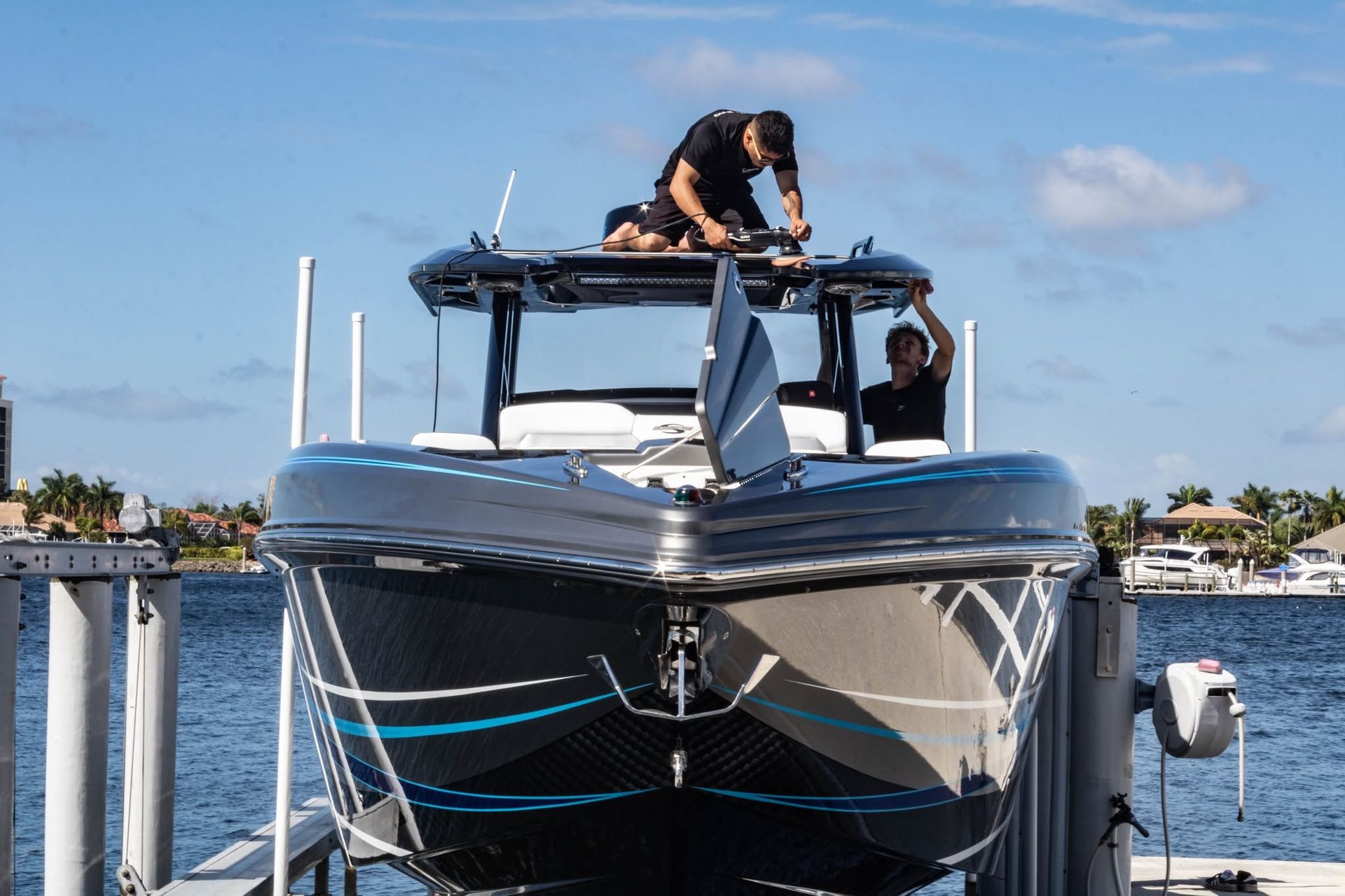 Yacht at dock with a person on the roof working on equipment, water and houses in the background