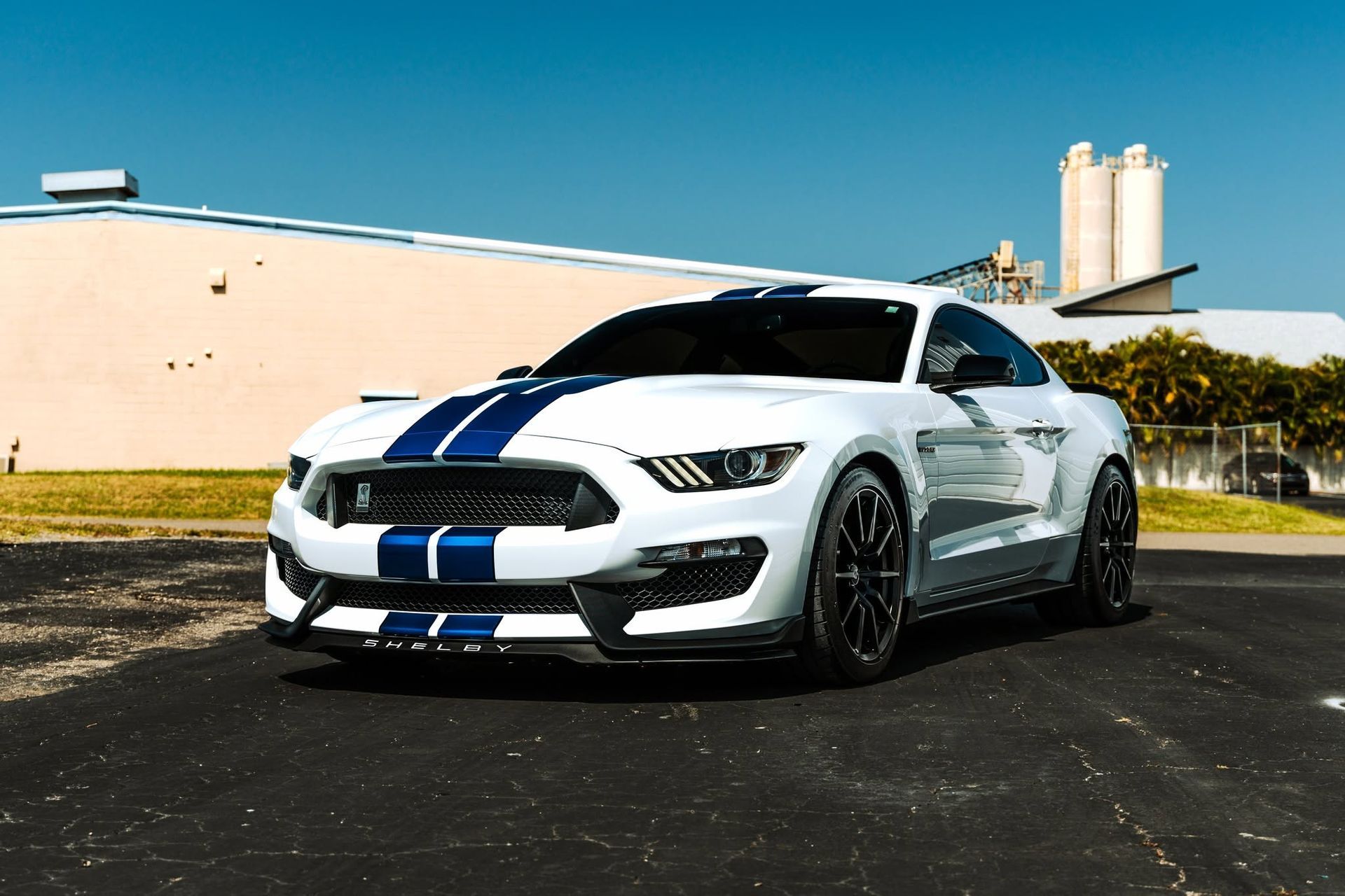 White sports car with blue racing stripes parked on asphalt near a beige building