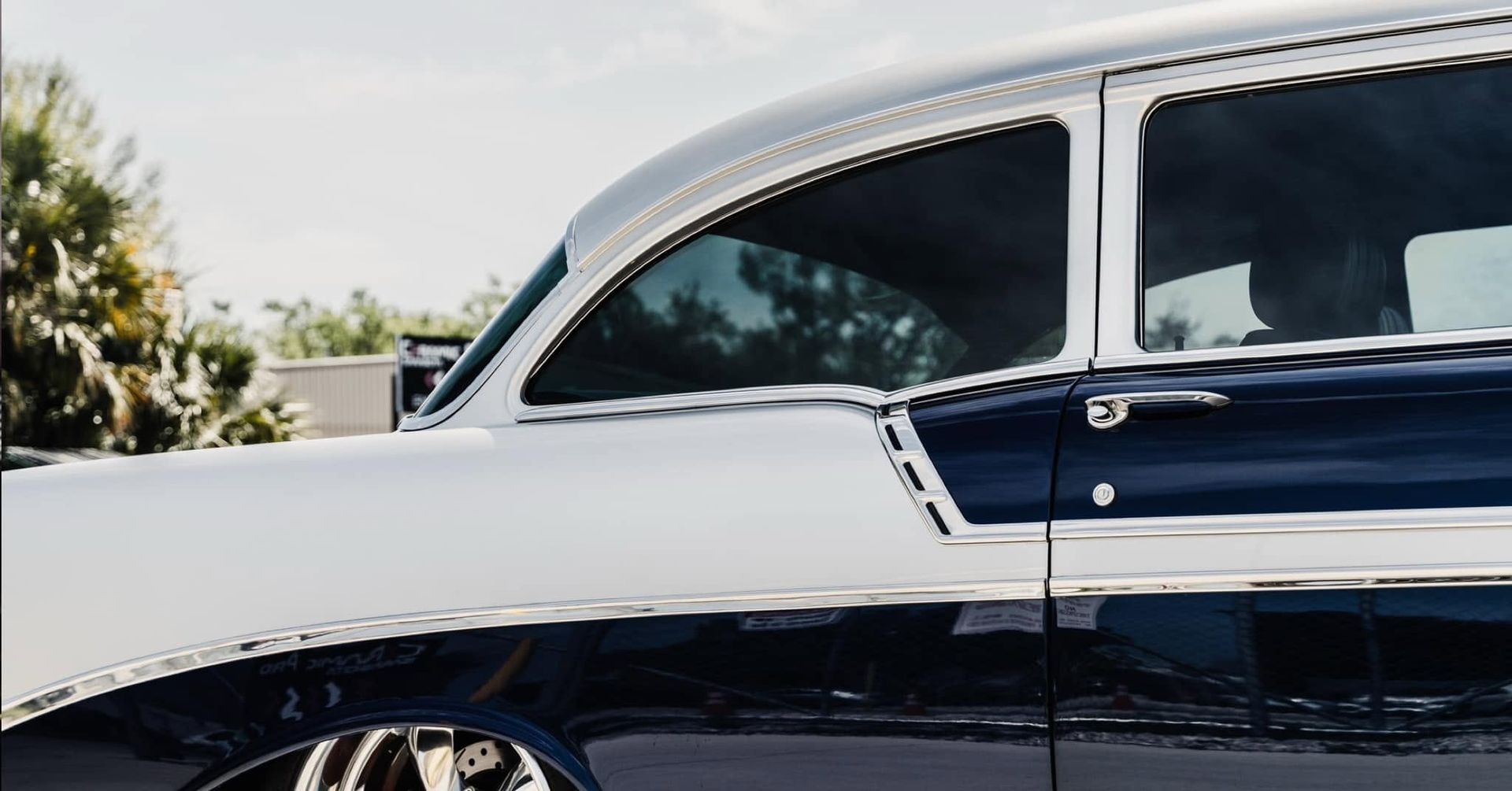 Side view of a two-tone black and white classic car parked outdoors in sunlight