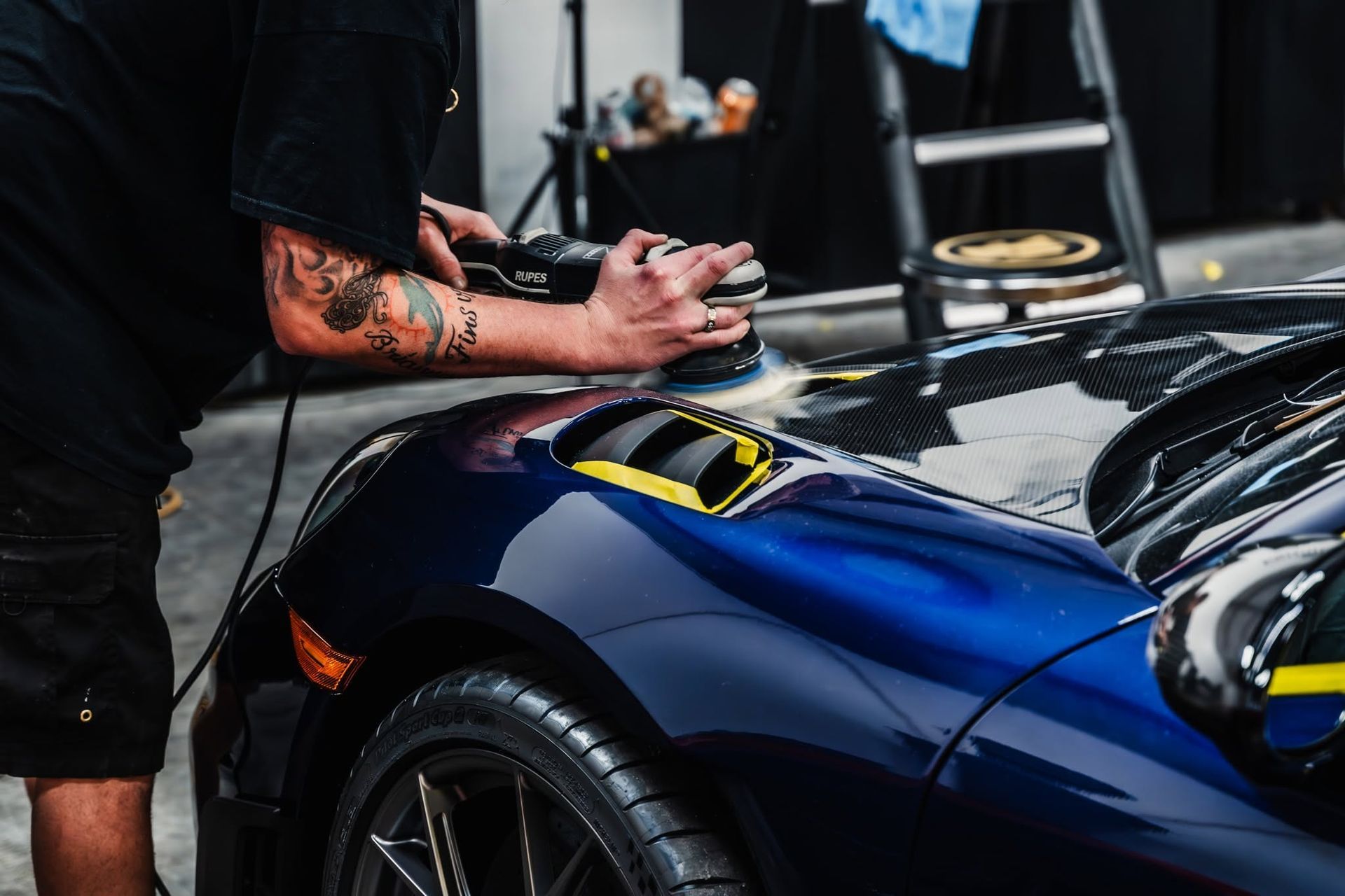 Detailing a blue sports car as a person polishes the hood and fender with a cloth