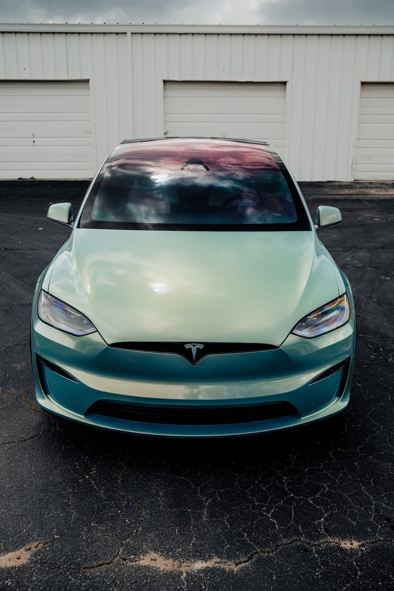 Front view of a mint green Tesla parked on wet pavement in front of white garage doors.