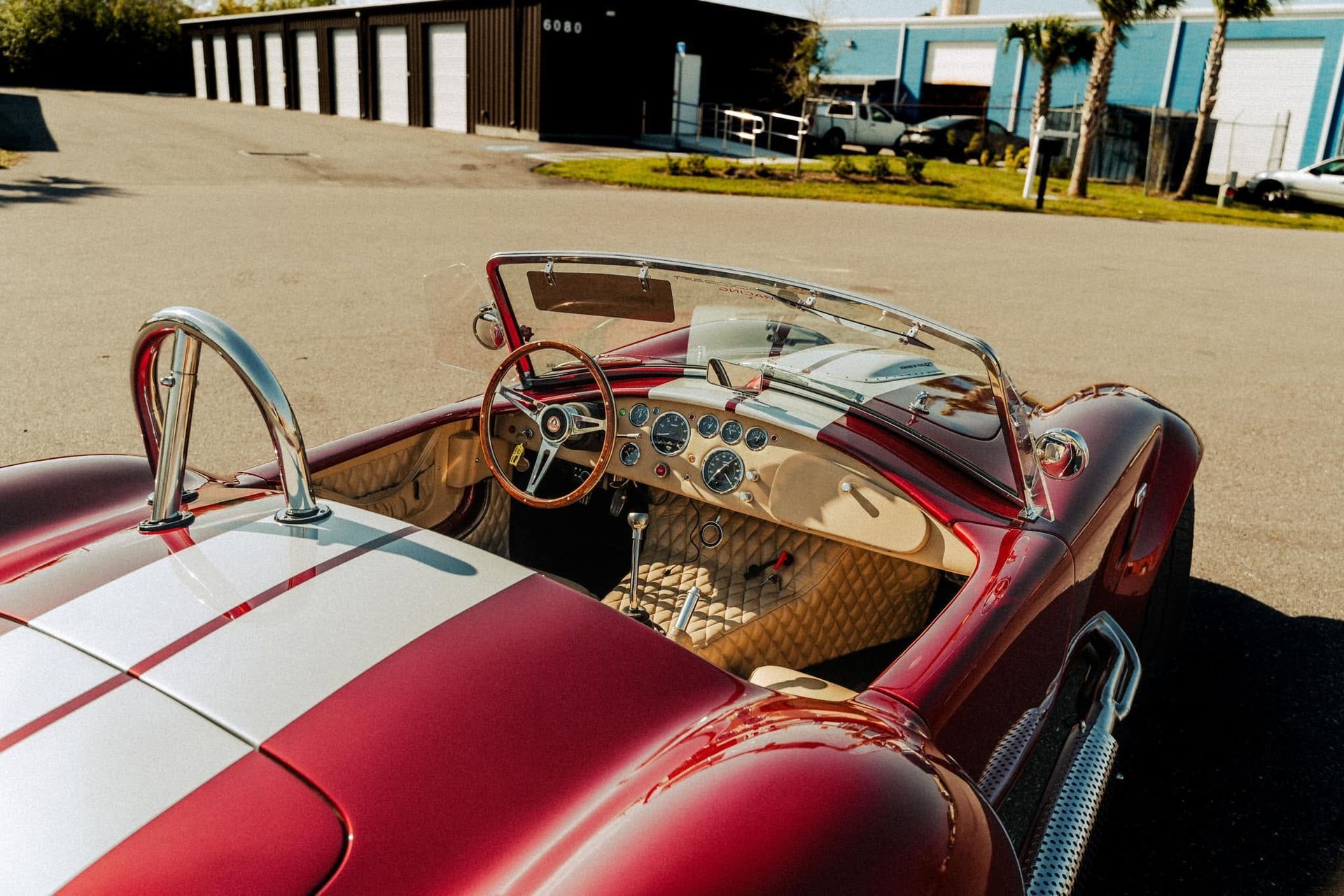Red vintage convertible with white racing stripes parked outdoors near buildings