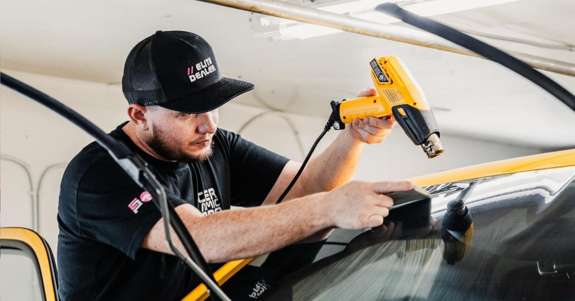 Worker using a yellow heat gun to repair a car windshield in a garage