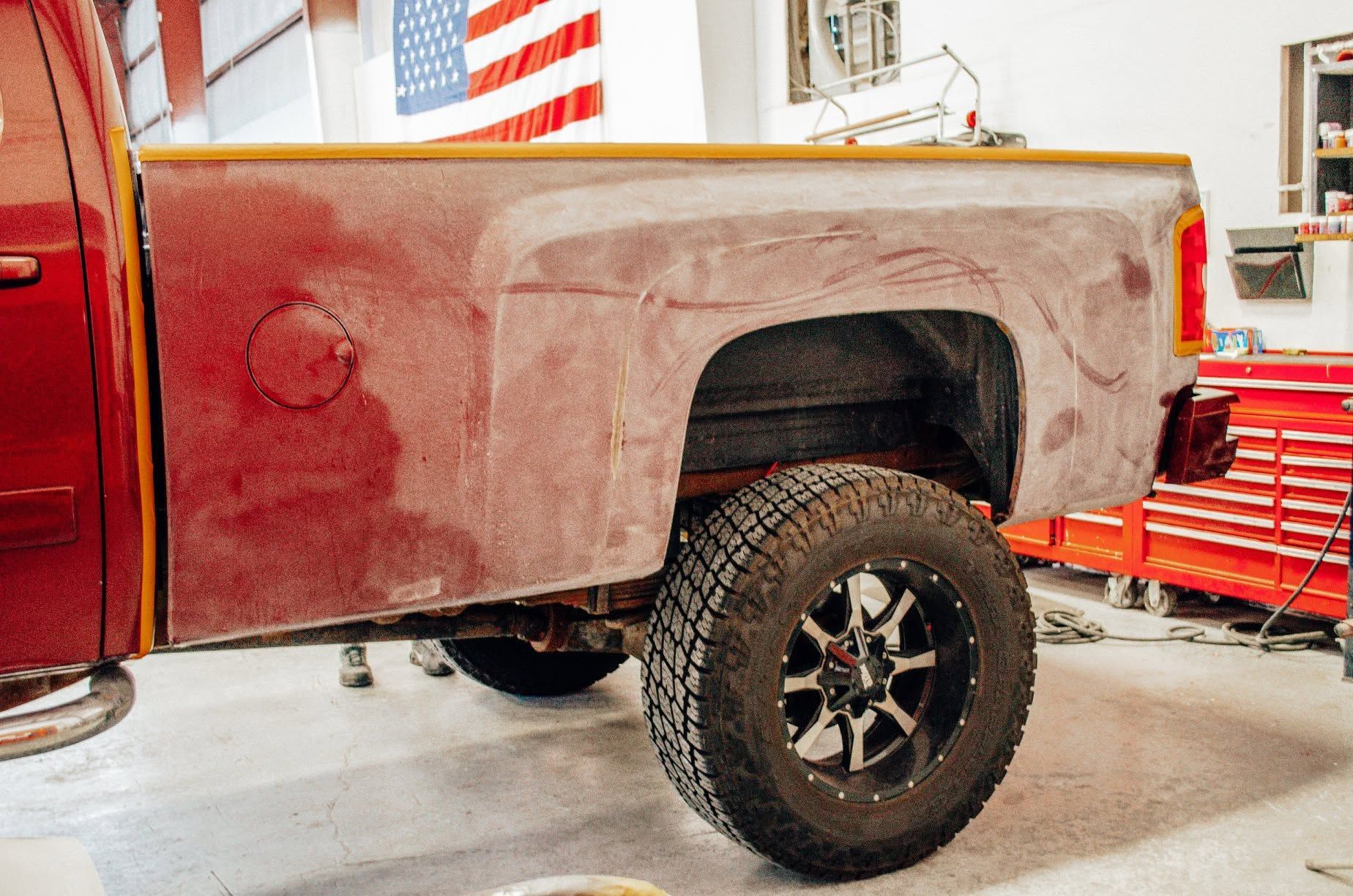 Red pickup truck bed in a workshop, with a rear wheel and tools in the background