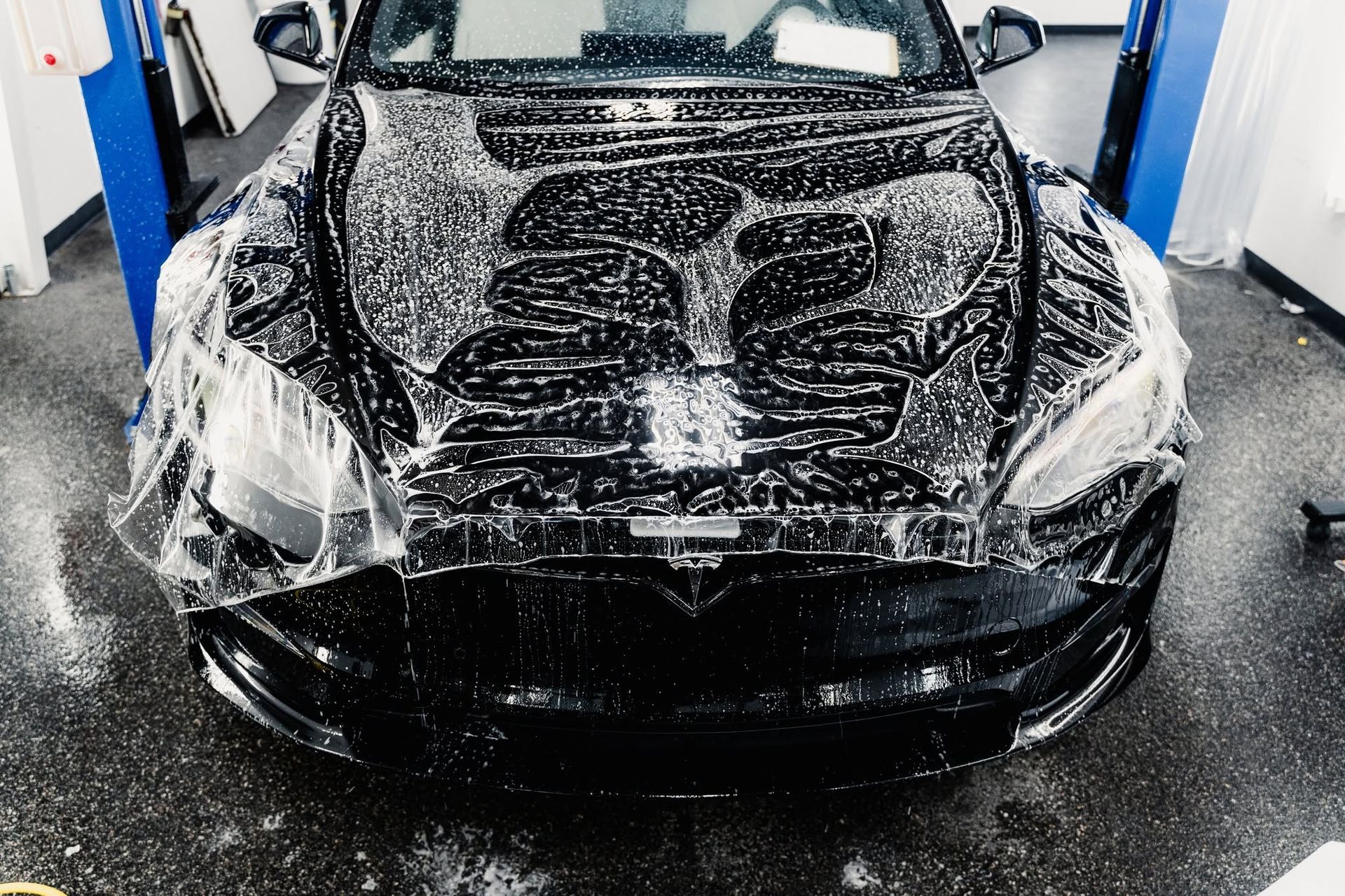 Black car covered in soap suds being washed in a car detailing bay