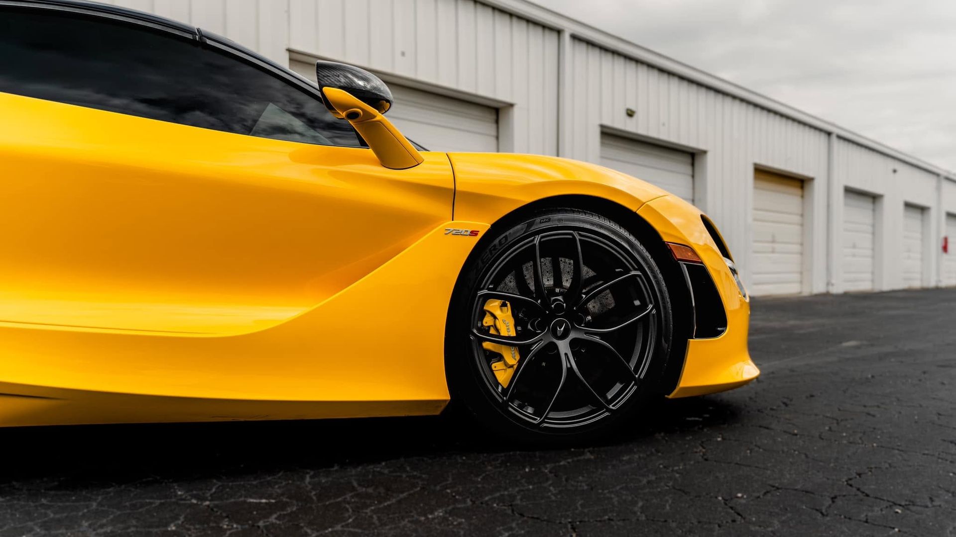 Yellow sports car parked beside white garage doors on wet pavement, close-up of front side and wheel