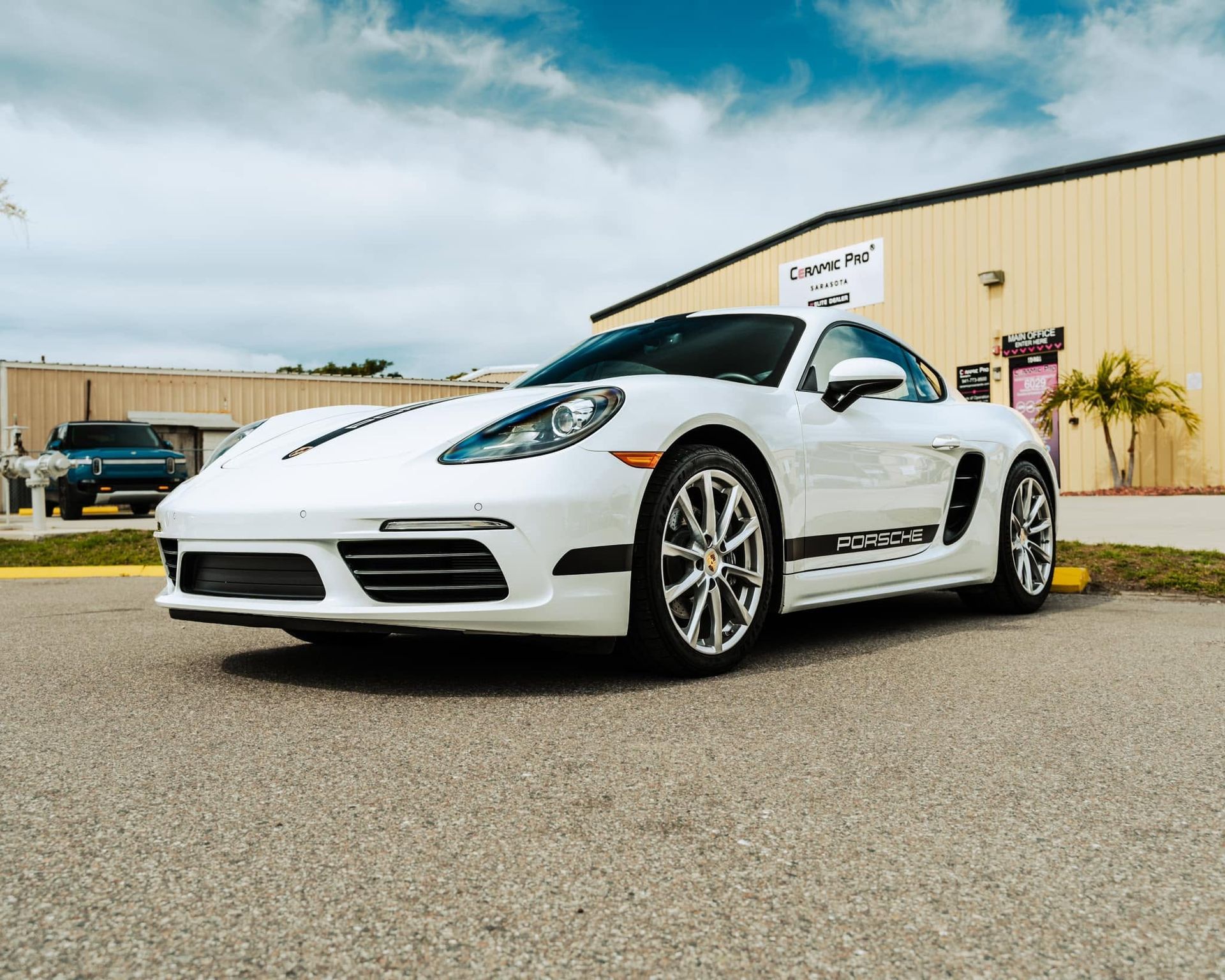 White sports car parked outside a tan building under a cloudy sky