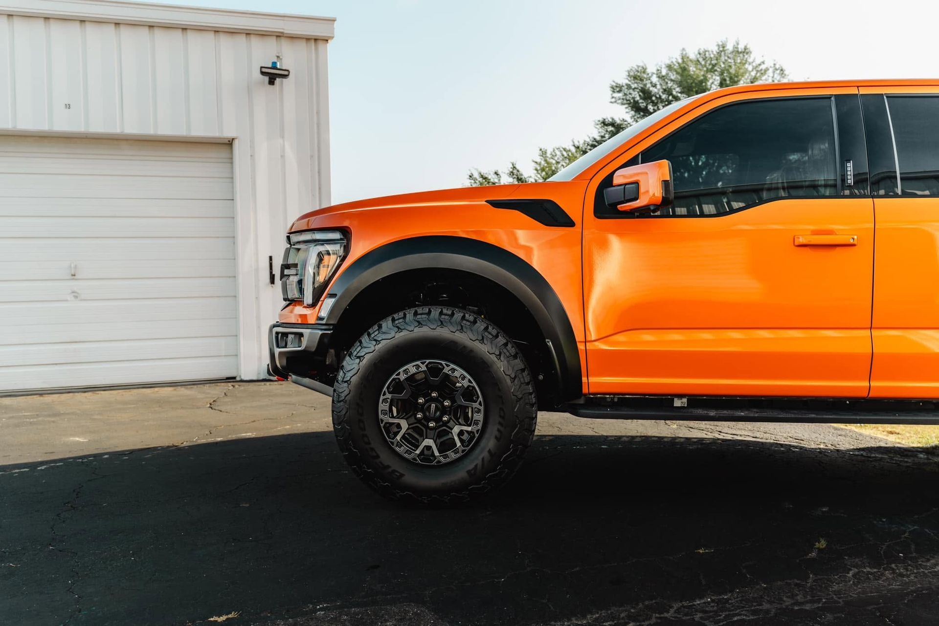 Orange pickup truck parked beside a white garage on a paved driveway