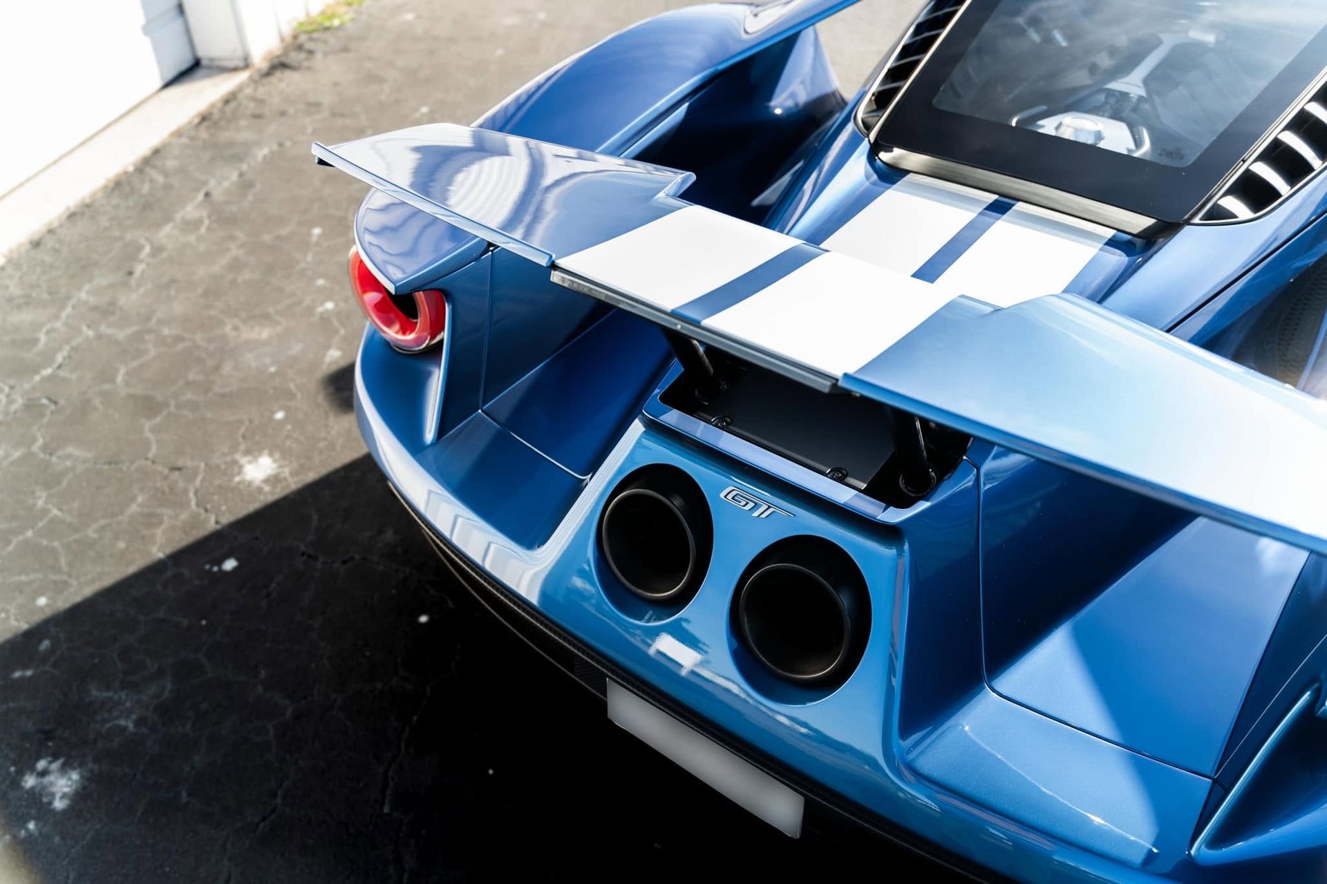 Rear view of a blue sports car with a large spoiler and twin exhausts on a concrete surface
