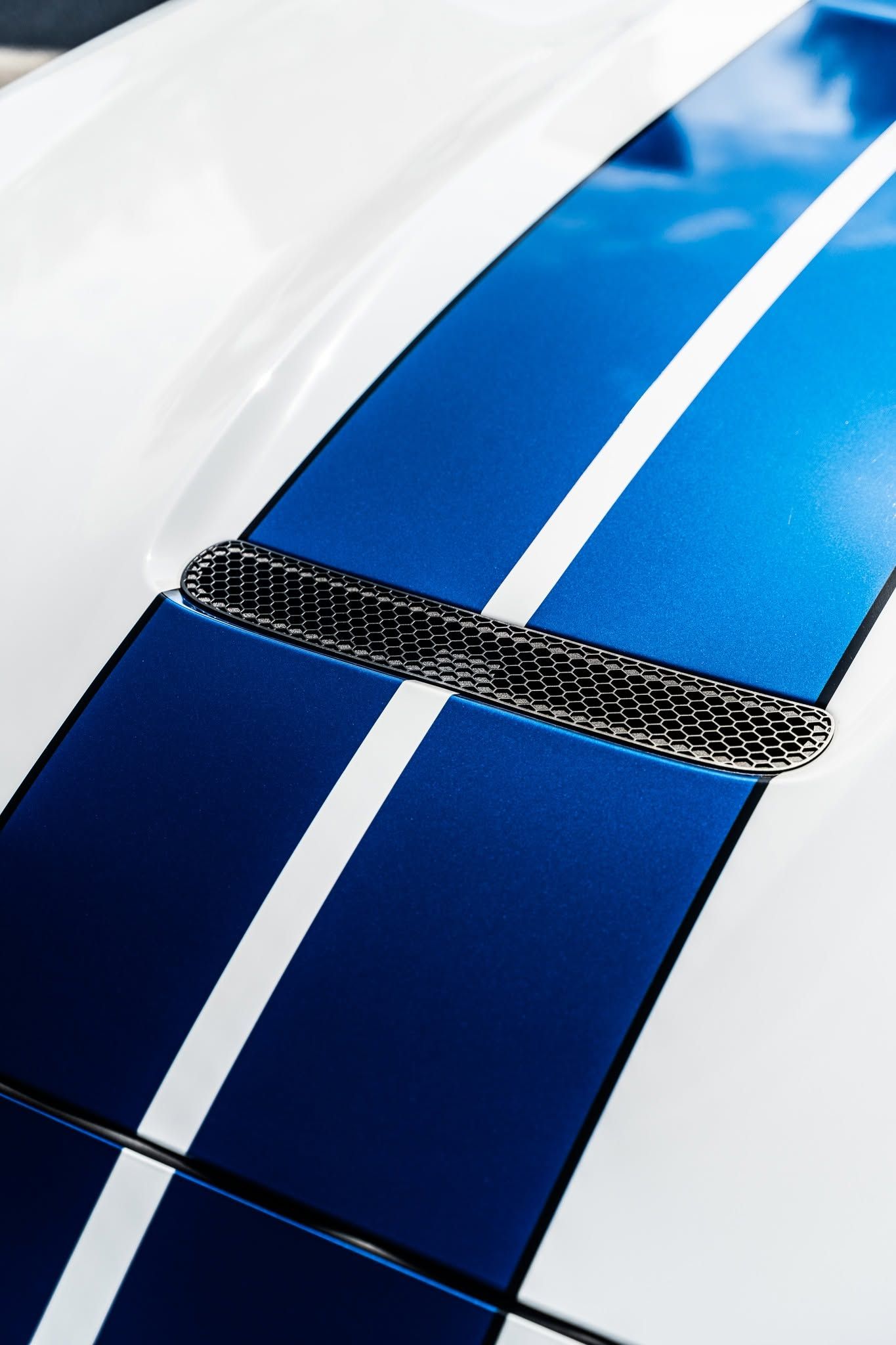 Close-up of a white car with blue racing stripes and a black hood scoop.