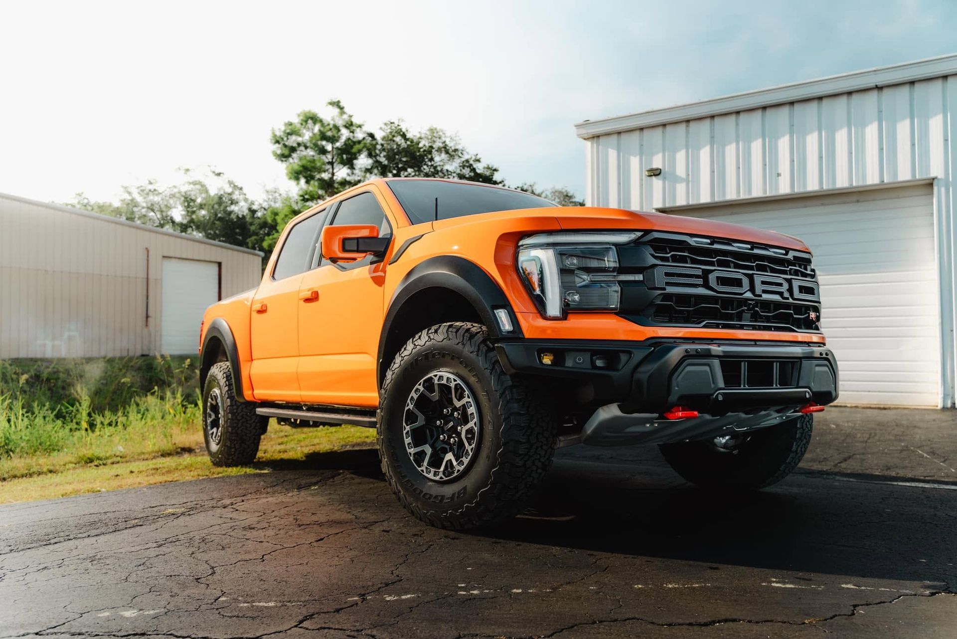 Bright orange off-road pickup truck parked outside a metal garage on a wet driveway