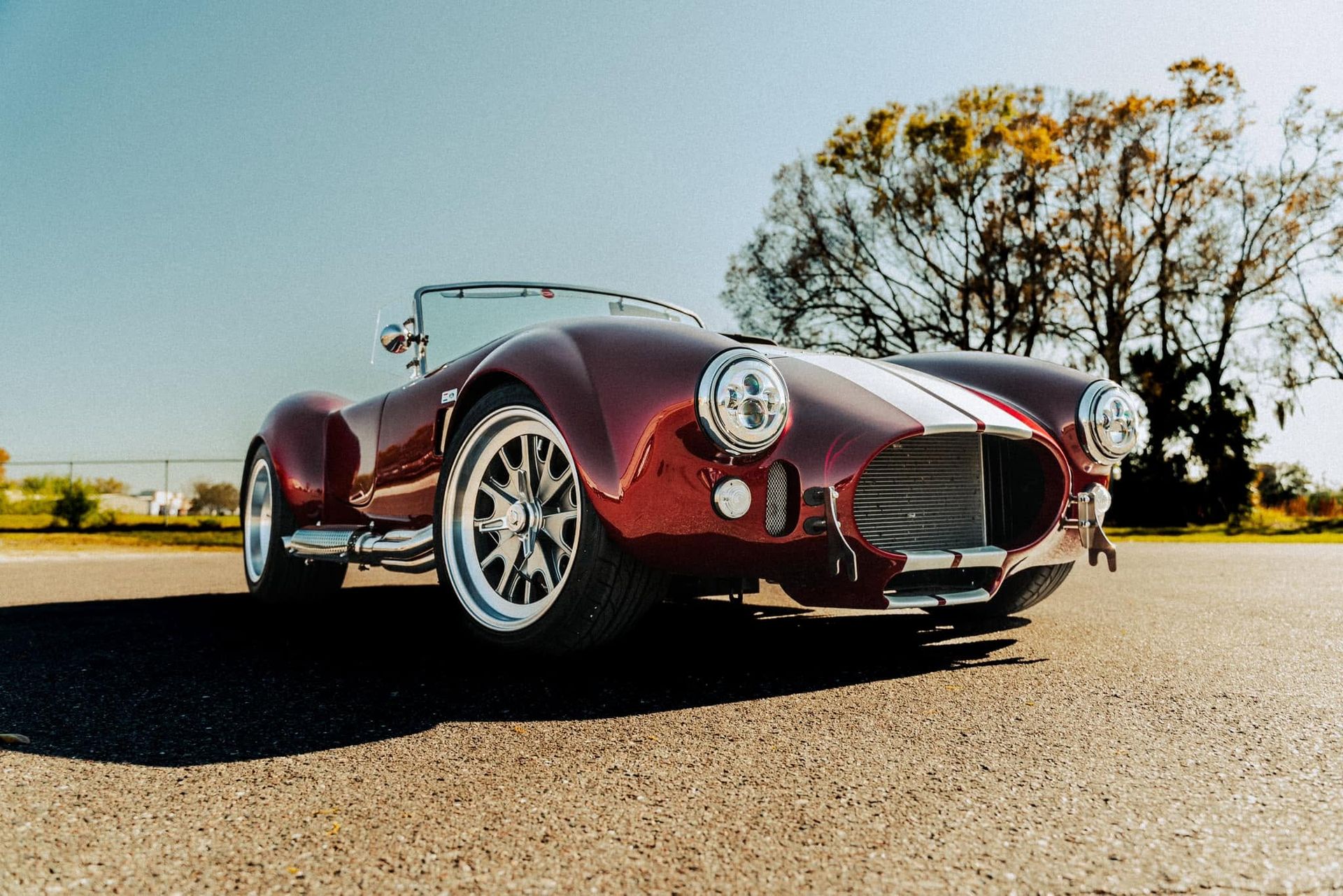 Maroon vintage sports car parked on a sunny road with trees in the background