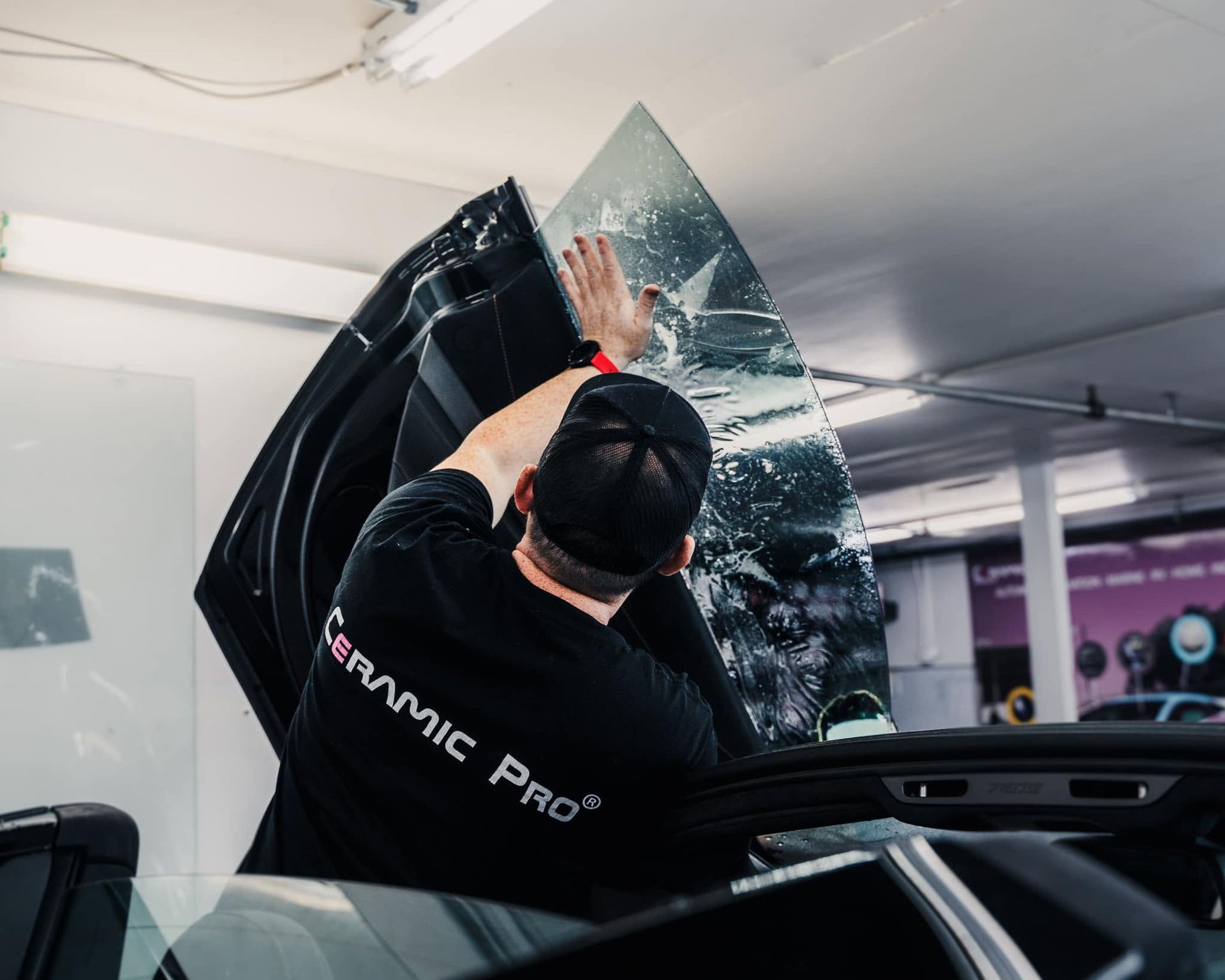 Technician installing a tinted windshield on a car in a garage