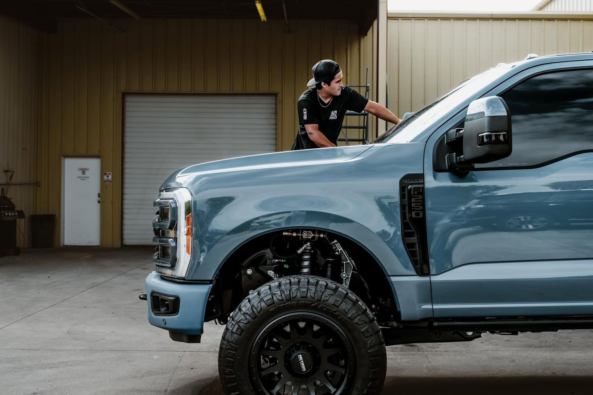 Man leaning on a blue lifted pickup truck in an industrial garage