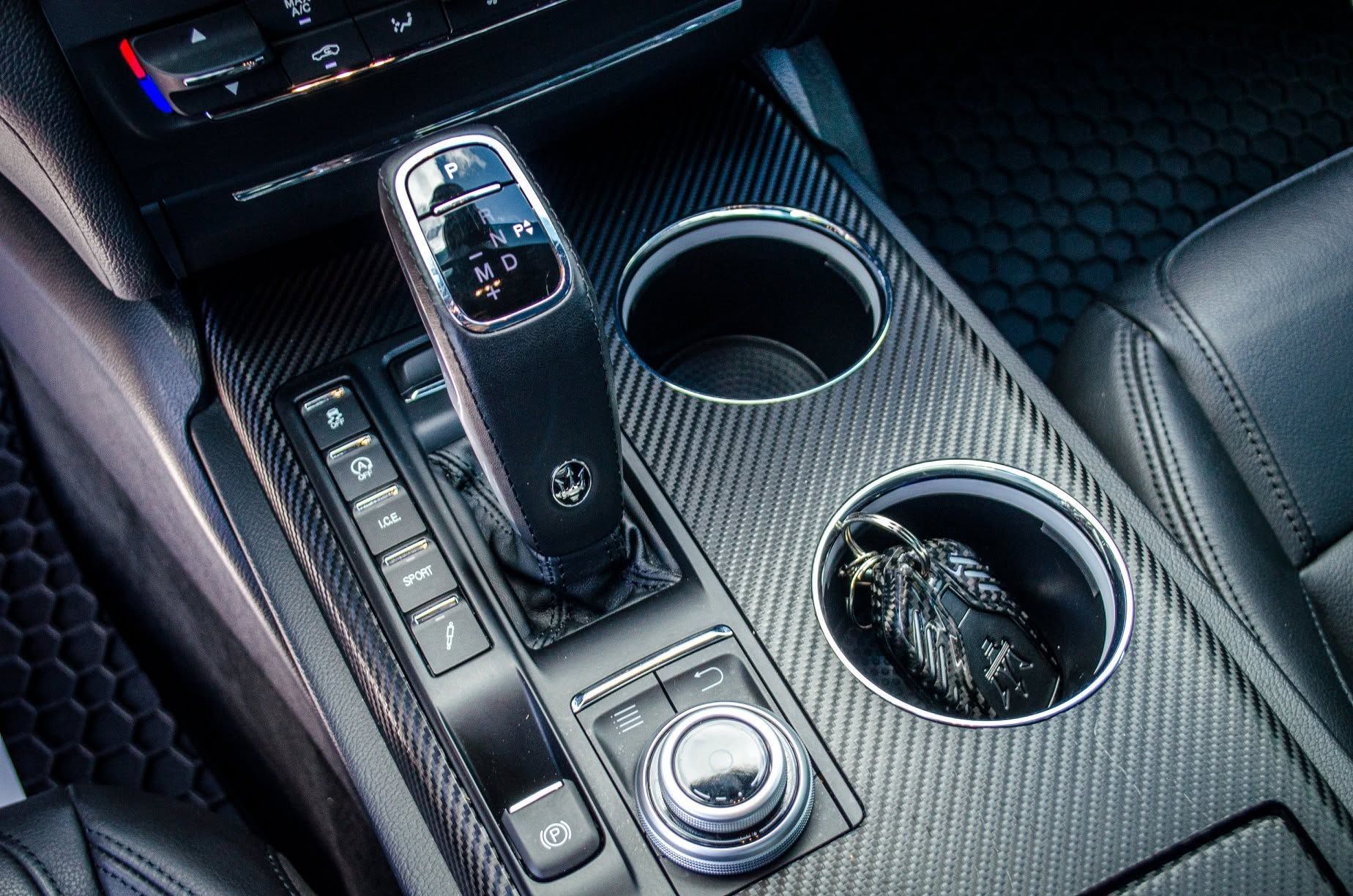 Car center console with gear shifter, cup holders, and carbon-fiber trim in dark interior