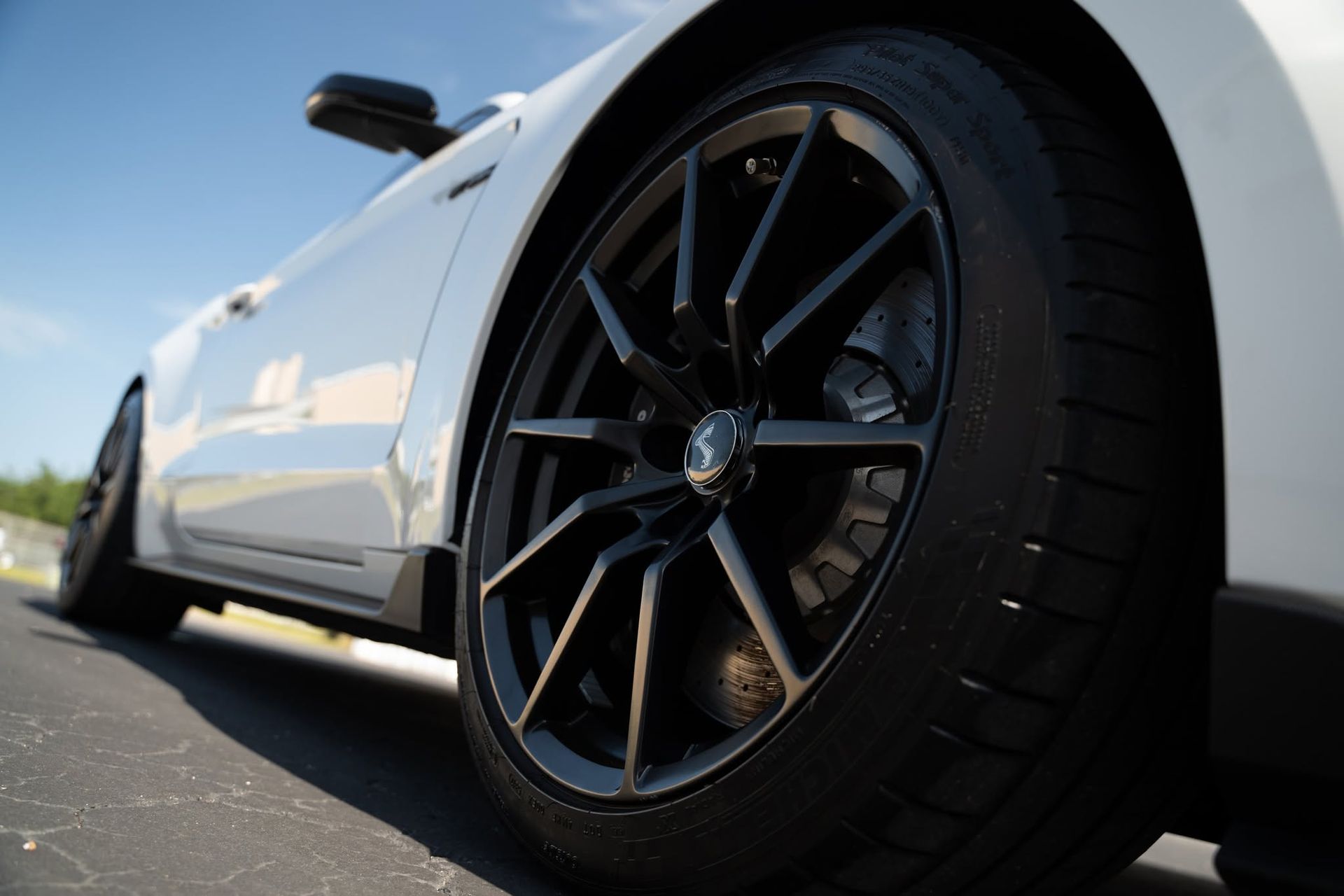 Low-angle view of a white sports car with black alloy wheel parked on a road
