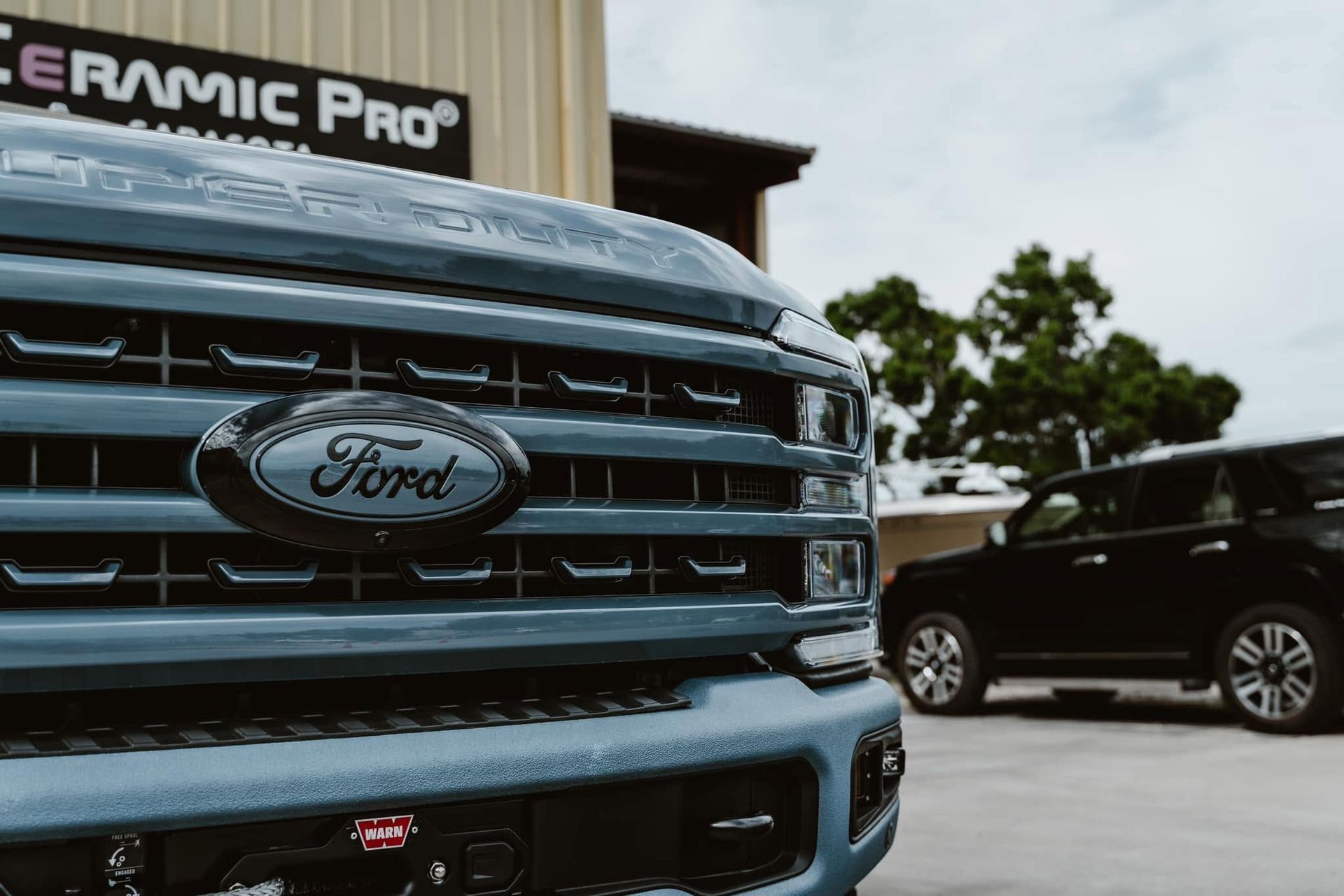 Close-up of a blue Ford truck grille with a black SUV parked in the background