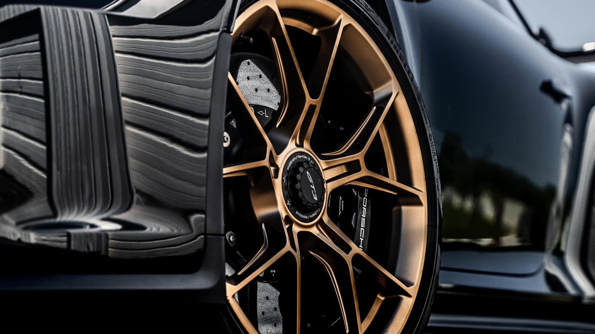 Close-up of a black sports car with bronze alloy wheel and carbon-fiber detailing.