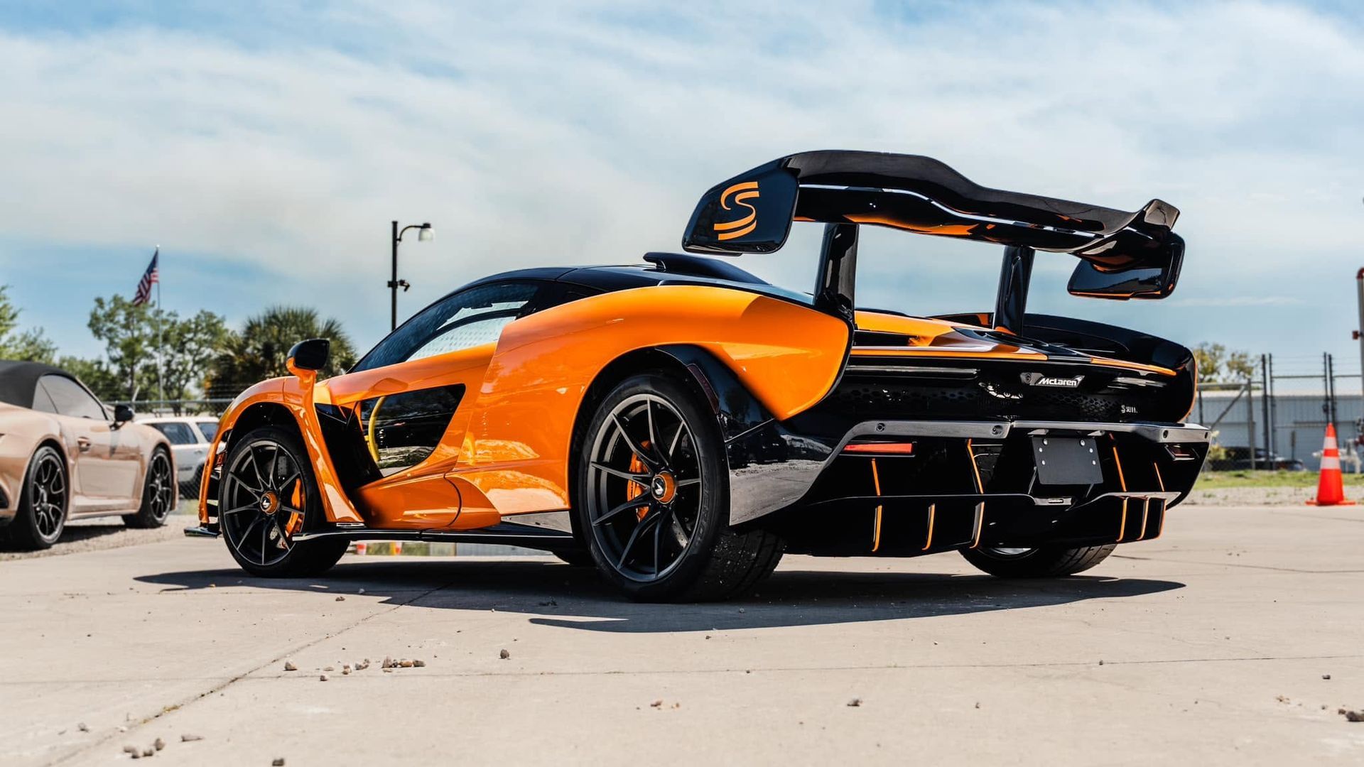 Orange sports car with black spoiler parked outdoors on a sunny day