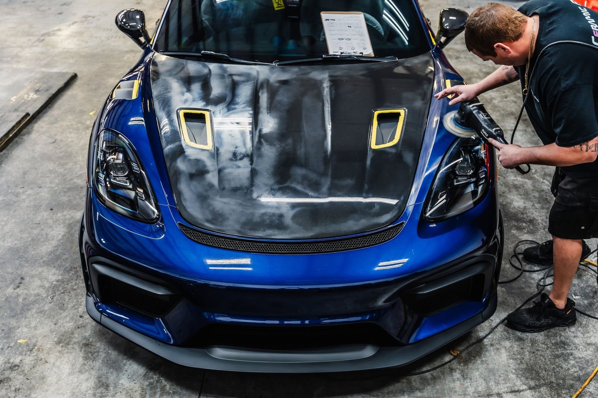 Blue sports car with carbon-fiber hood being worked on in a garage
