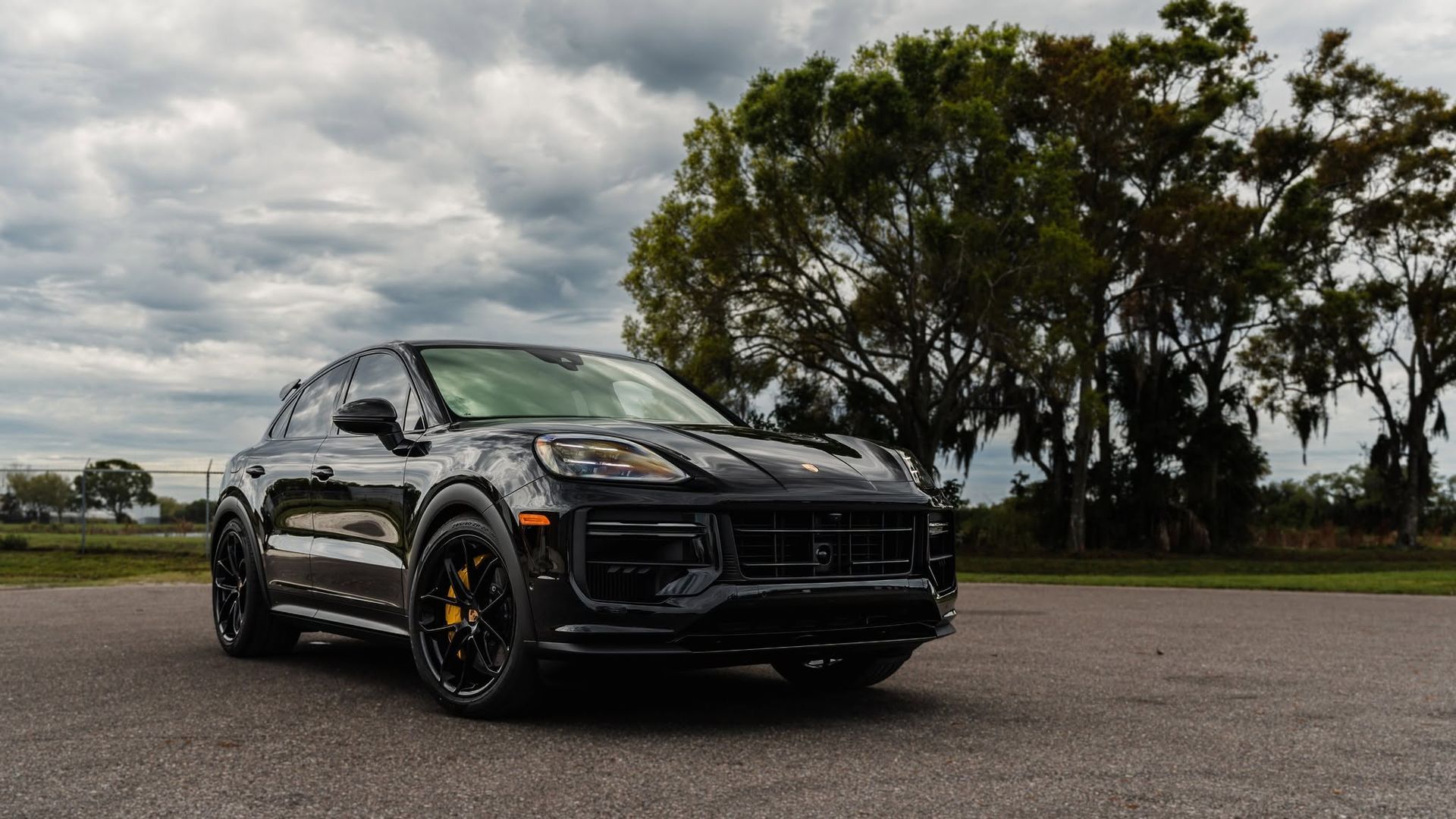 Black Porsche SUV parked on a road under cloudy skies, with trees in the background