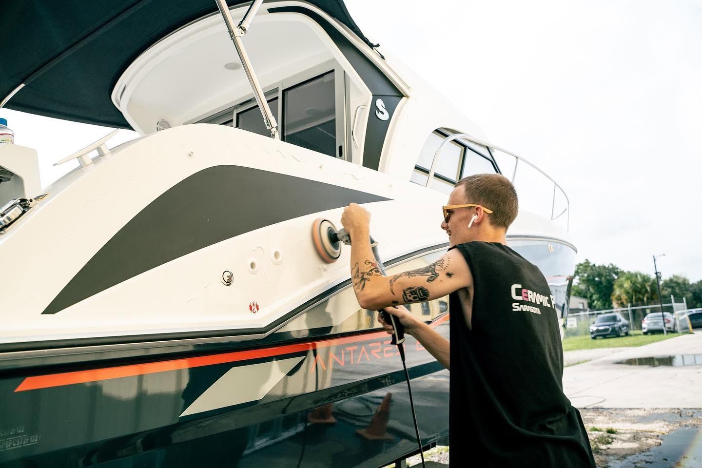 Man polishing the bow of a white boat at a marina, wearing a black shirt and sunglasses