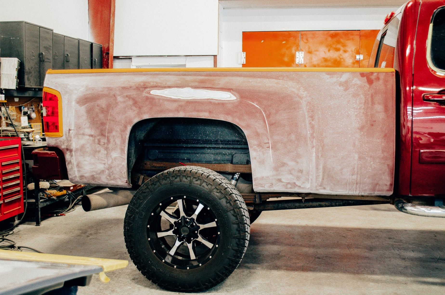 Red pickup truck with a primered rear quarter panel in a workshop garage