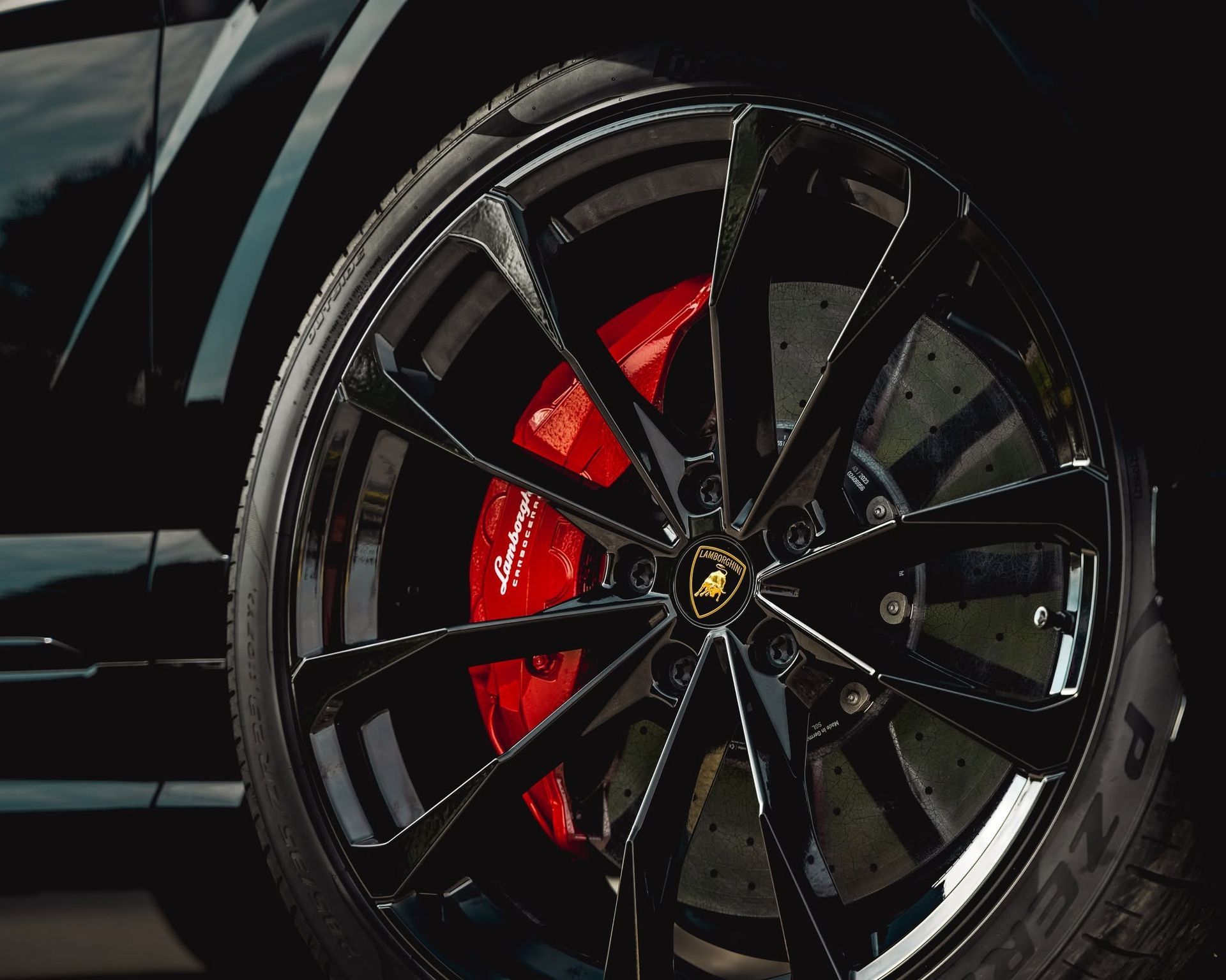 Close-up of a glossy black sports car wheel with a red brake caliper and gold emblem