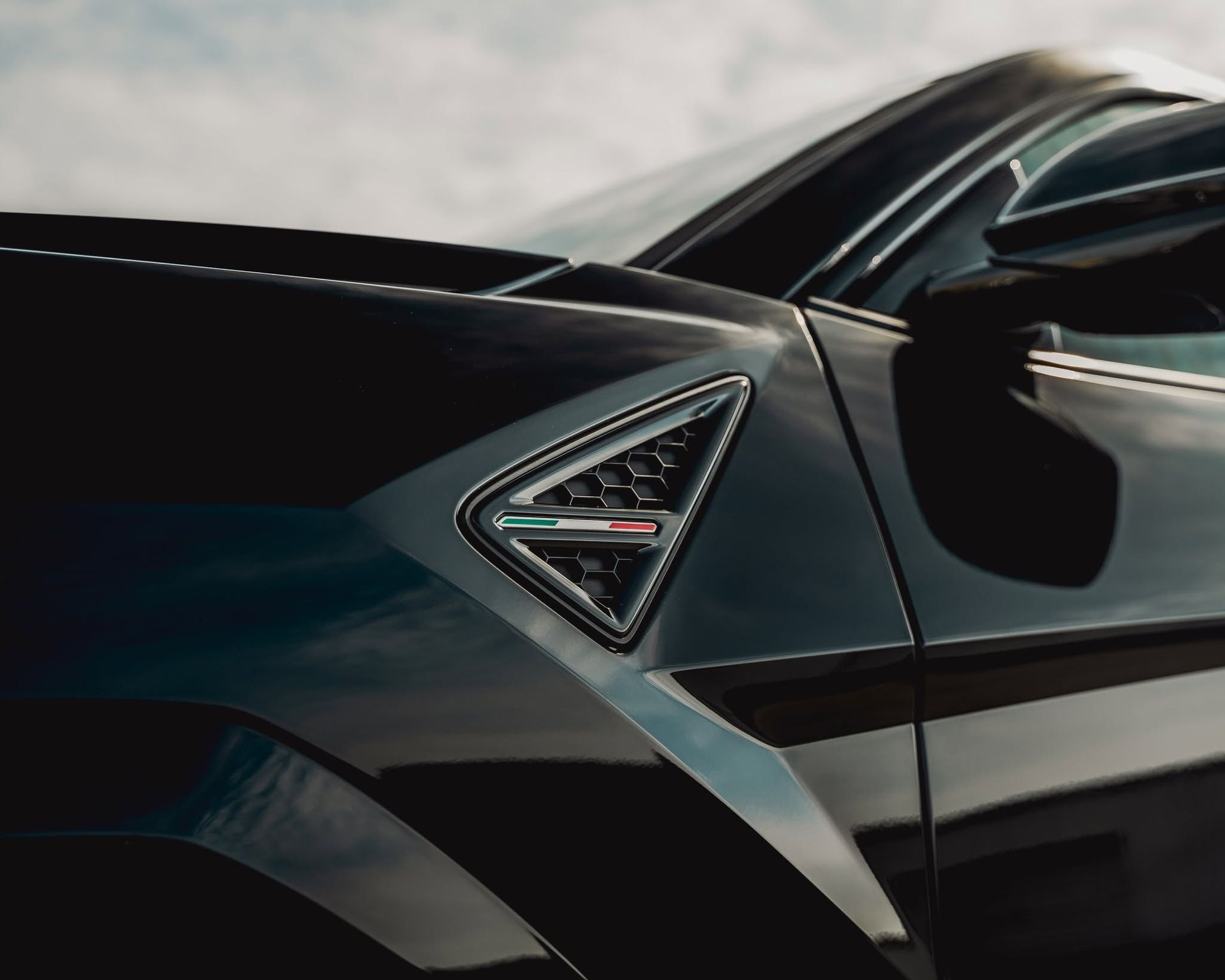 Close-up of a black sports car’s side vent and glossy bodywork under studio lighting