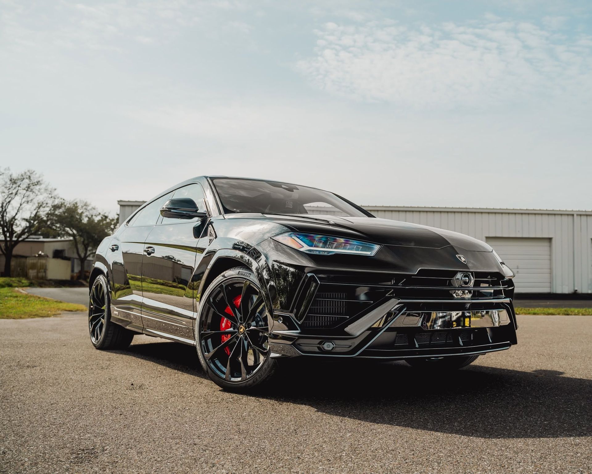 Black sports coupe parked on pavement beside a white building, with red brake calipers and glossy finish