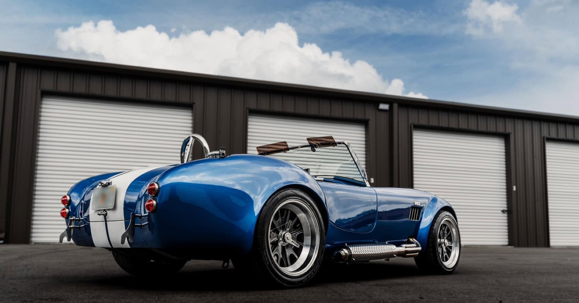 Blue classic Shelby Cobra roadster parked in front of white garage doors