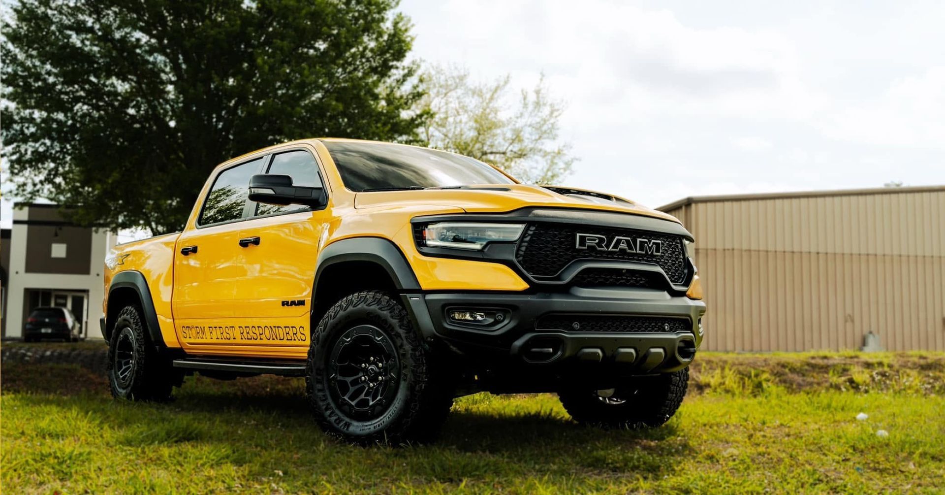 Yellow pickup truck parked on grass beside a beige building under cloudy skies