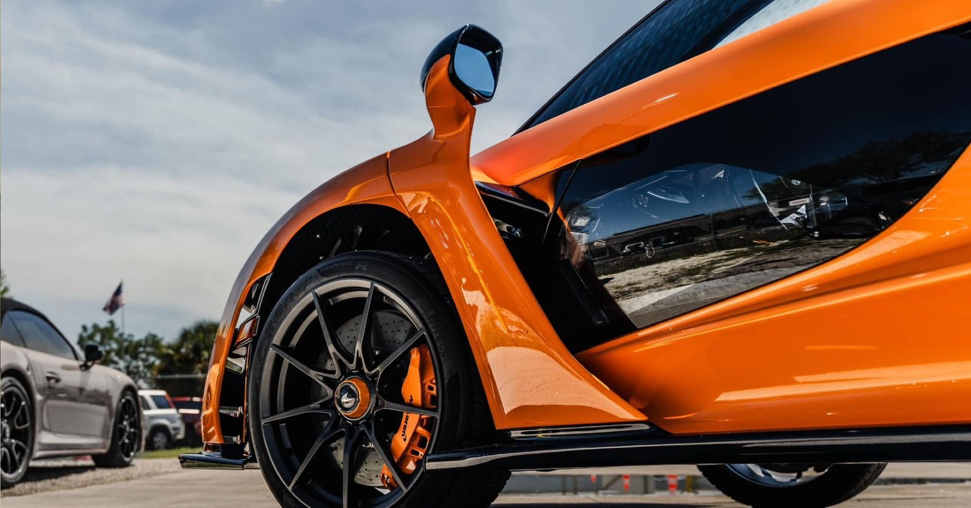 Orange sports car in low-angle view, showing front wheel and sleek side panel at a car meet