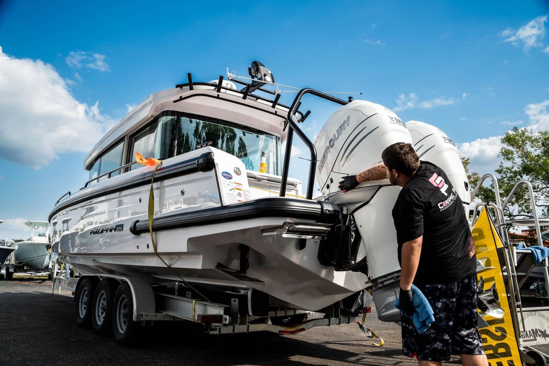 Man loading a white boat on a trailer at an outdoor marina under a blue sky