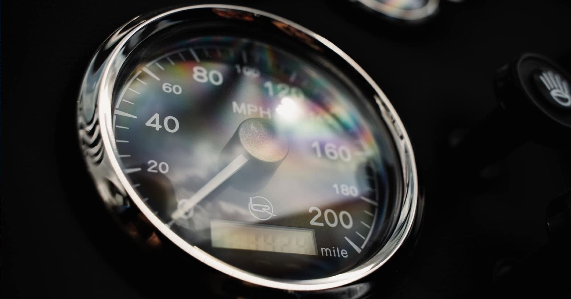 Close-up of a car dashboard speedometer, lit with reflections on a dark background